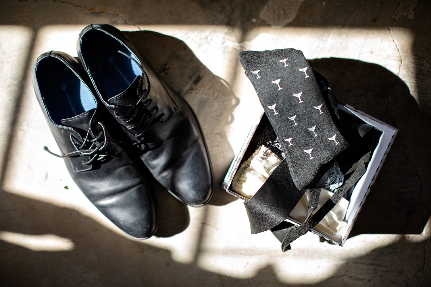 Groomsmens shoes, socks and tie gift box lie the light of the window in the grooms suite at The Rose Barn