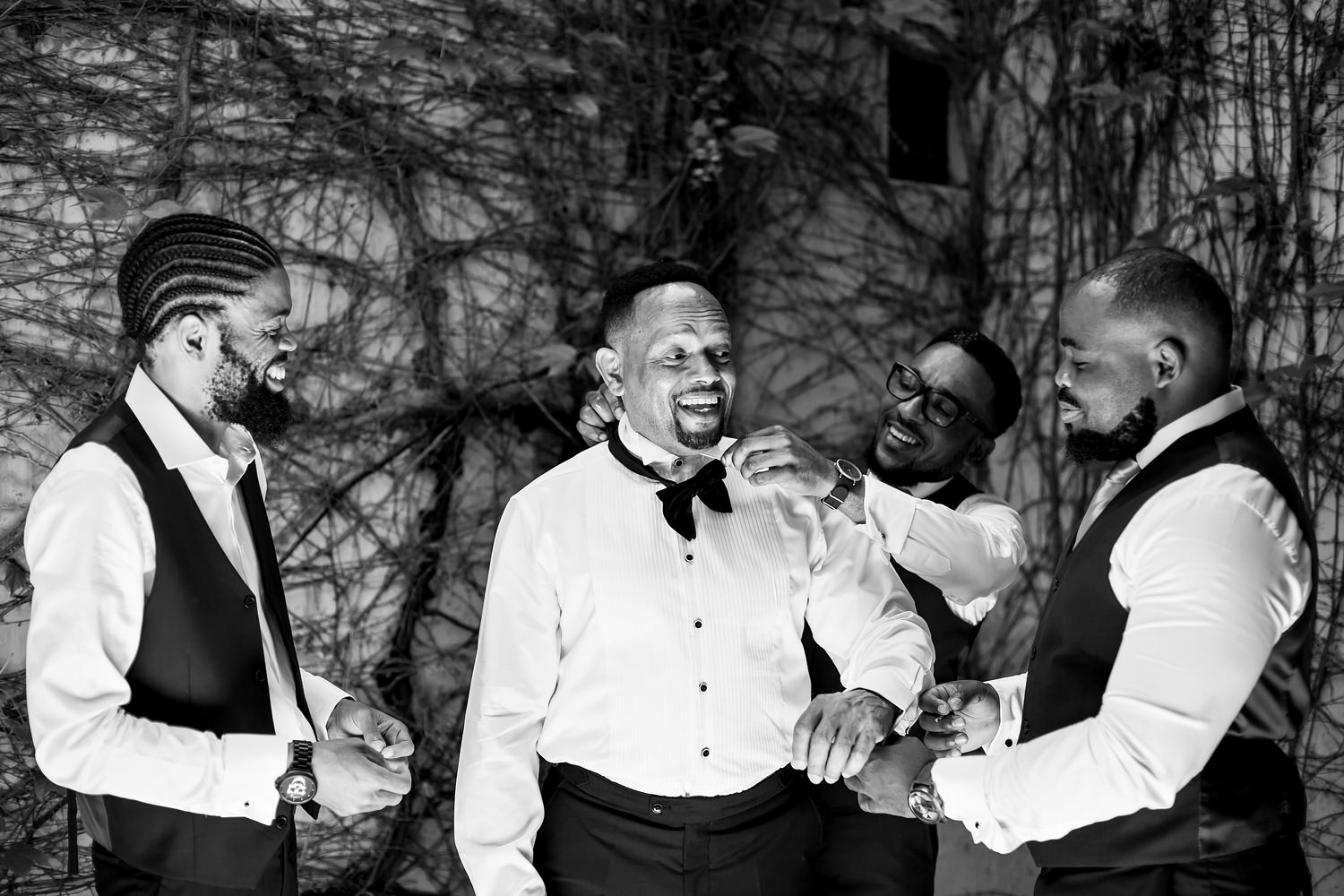 Black and white image of groomsmen dressing the groom