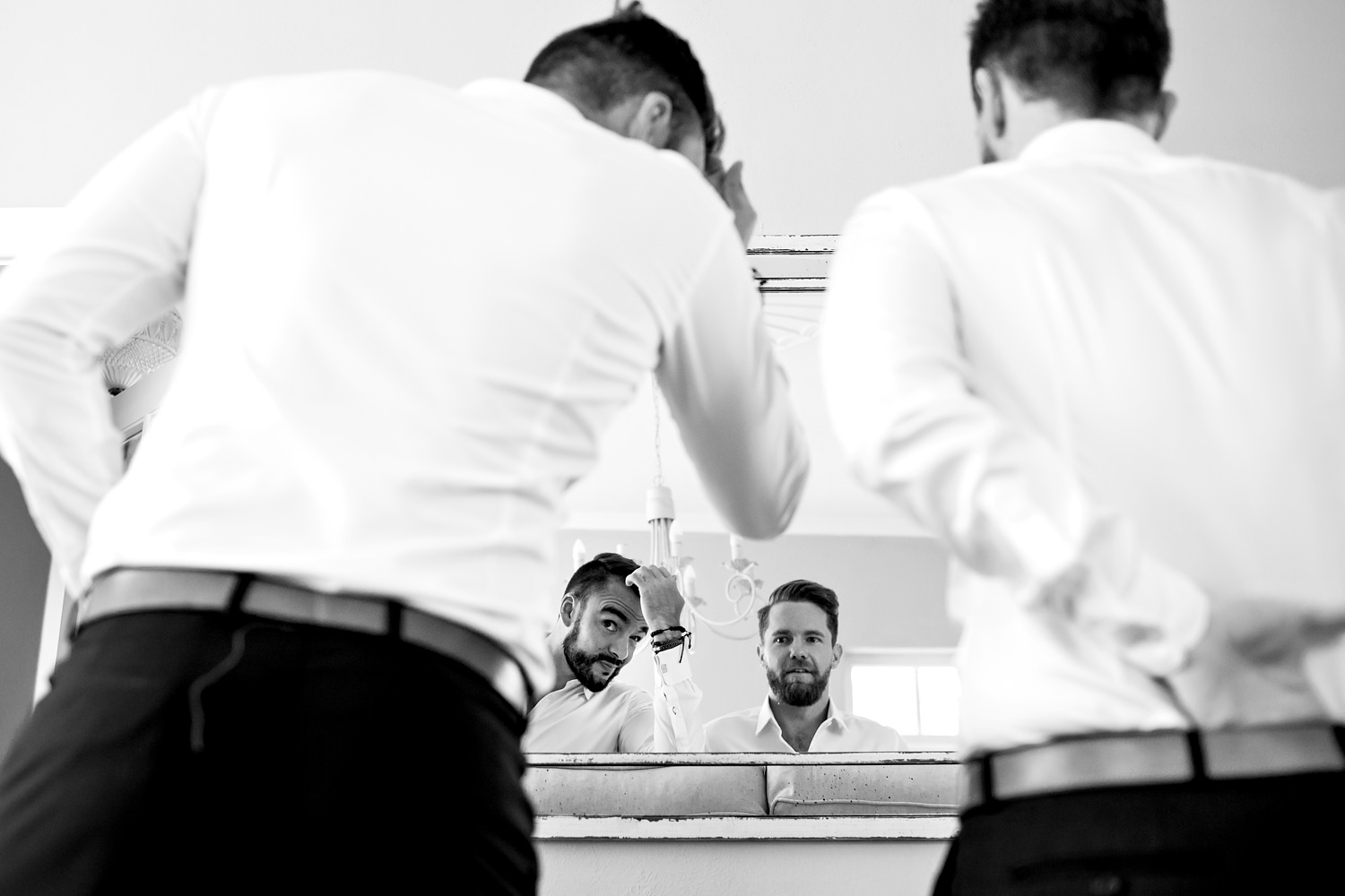Two groomsmen style their hair in a mirror