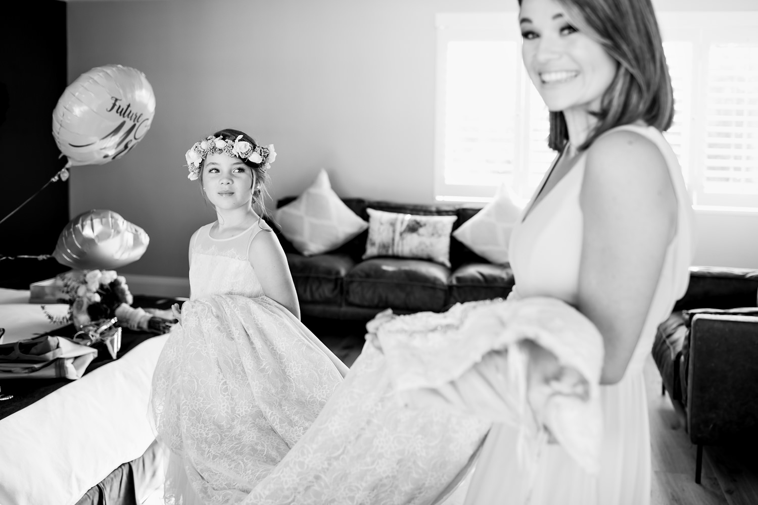 The flower girl looks at a smiling bridesmaid as they hold the wedding dress in preparation