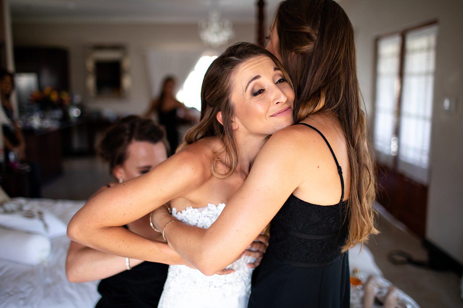 The smiling bride is held by her sister whilst one of the bridesmaids laces up the back of her corset gown