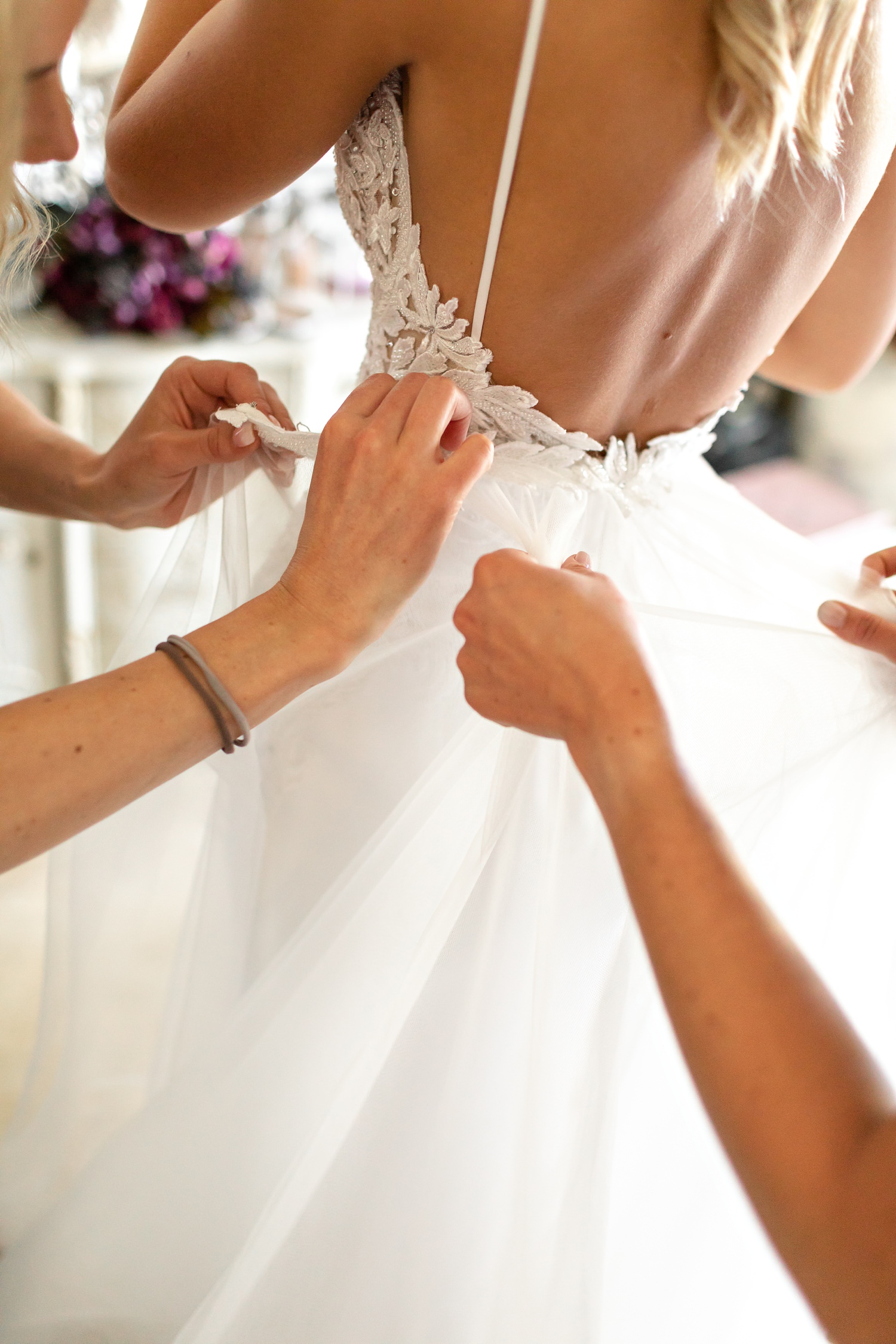 Bridesmaid hands hold a tuille overlay as it is attached to a Jason Kieck wedding dress