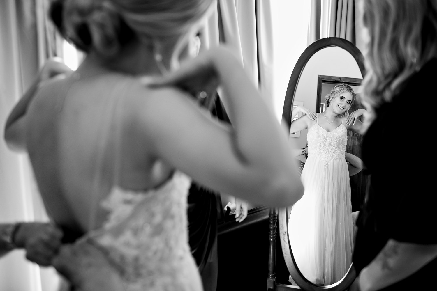Wedding photographer in South Africa captures the bride smiling as she looks at herself in the oval mirror whilst she is being dressed