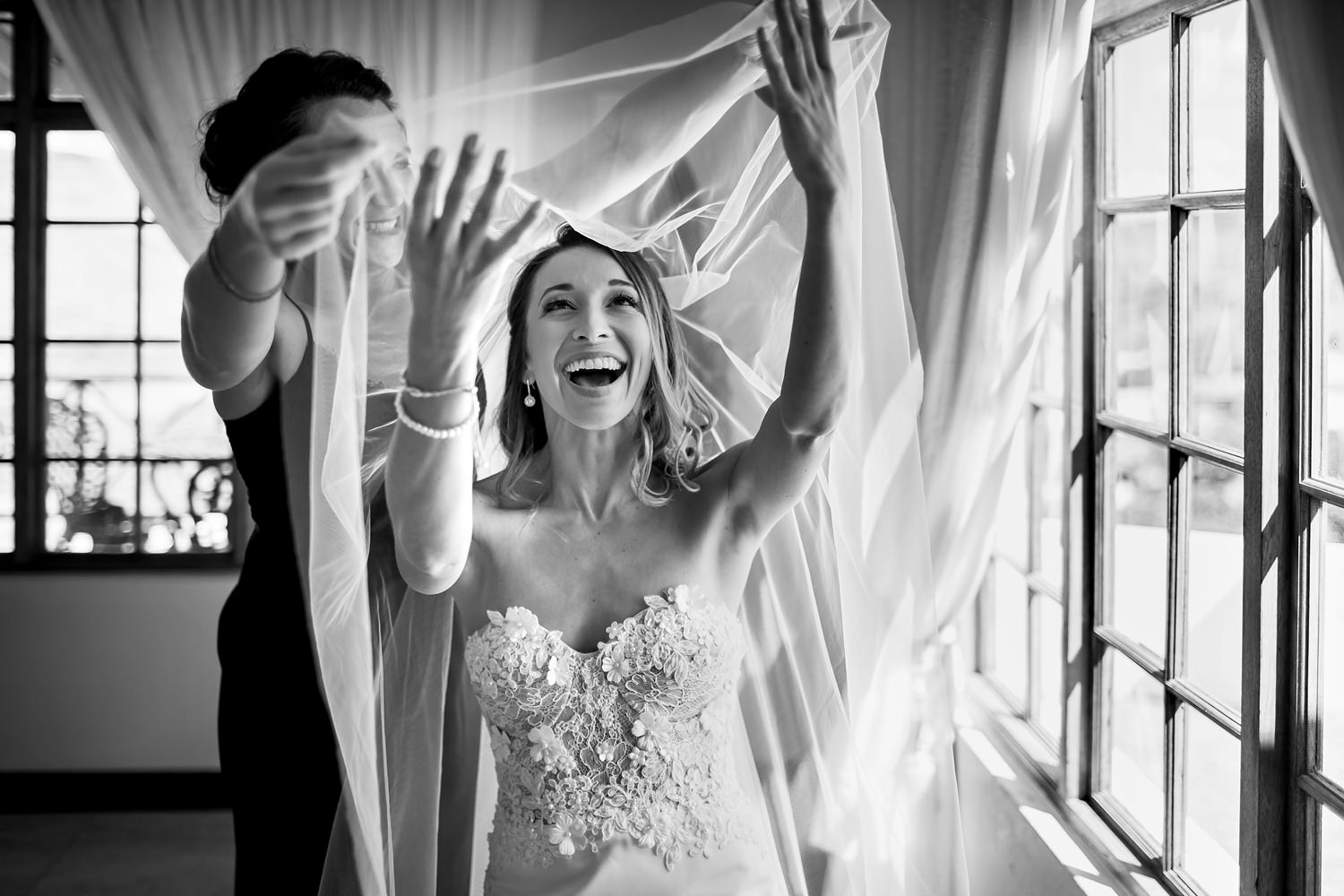 Niki M, a wedding photographer in South Africa, captures an elated bride laughing as her veil is lowered over her face, expressing pure joy at the thought of walking down the aisle and marrying her fiancé