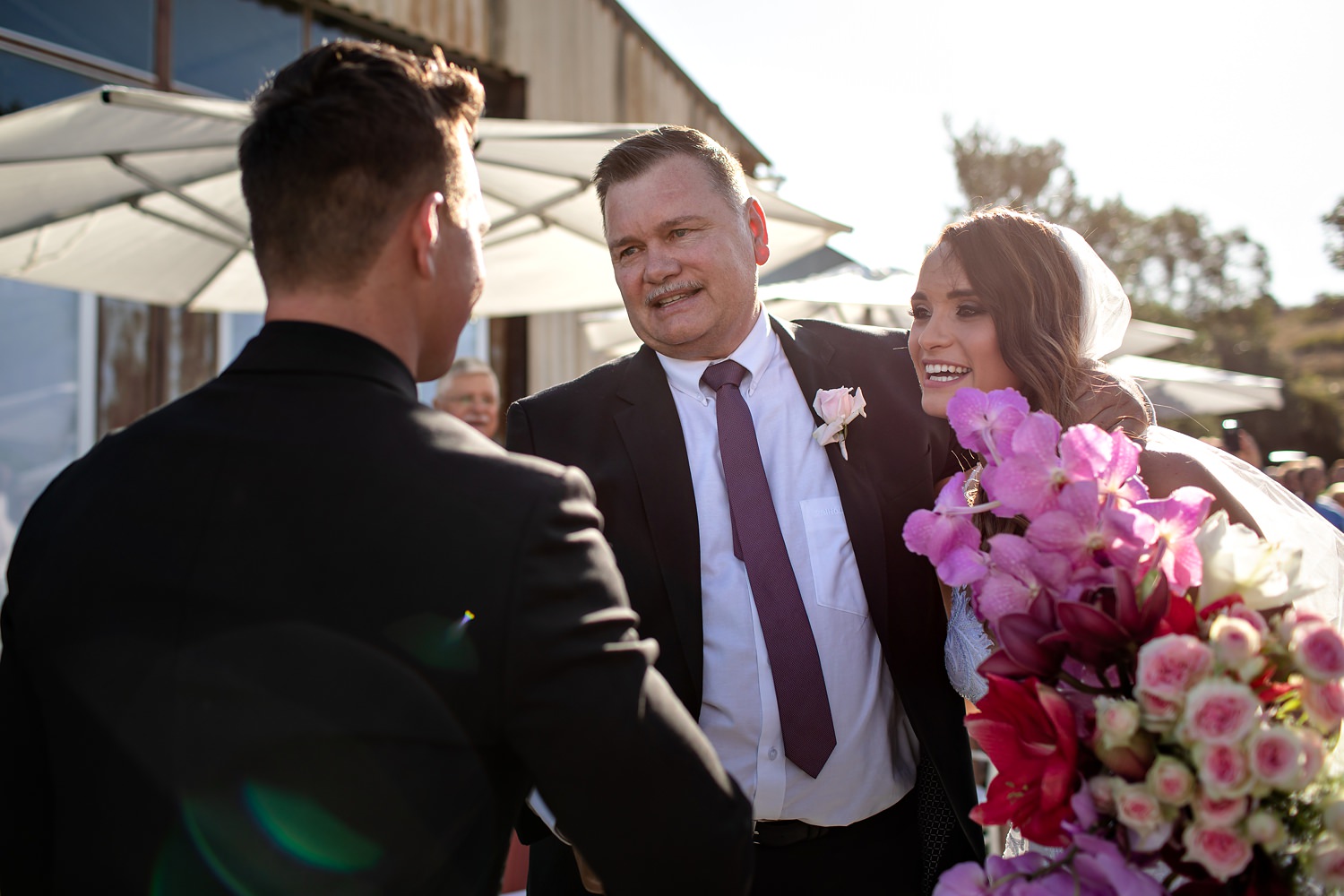 The bride's father shakes the grooms hand and embraces his daughter who holds a stunning cascading orchid bouquet by Otto de Jager