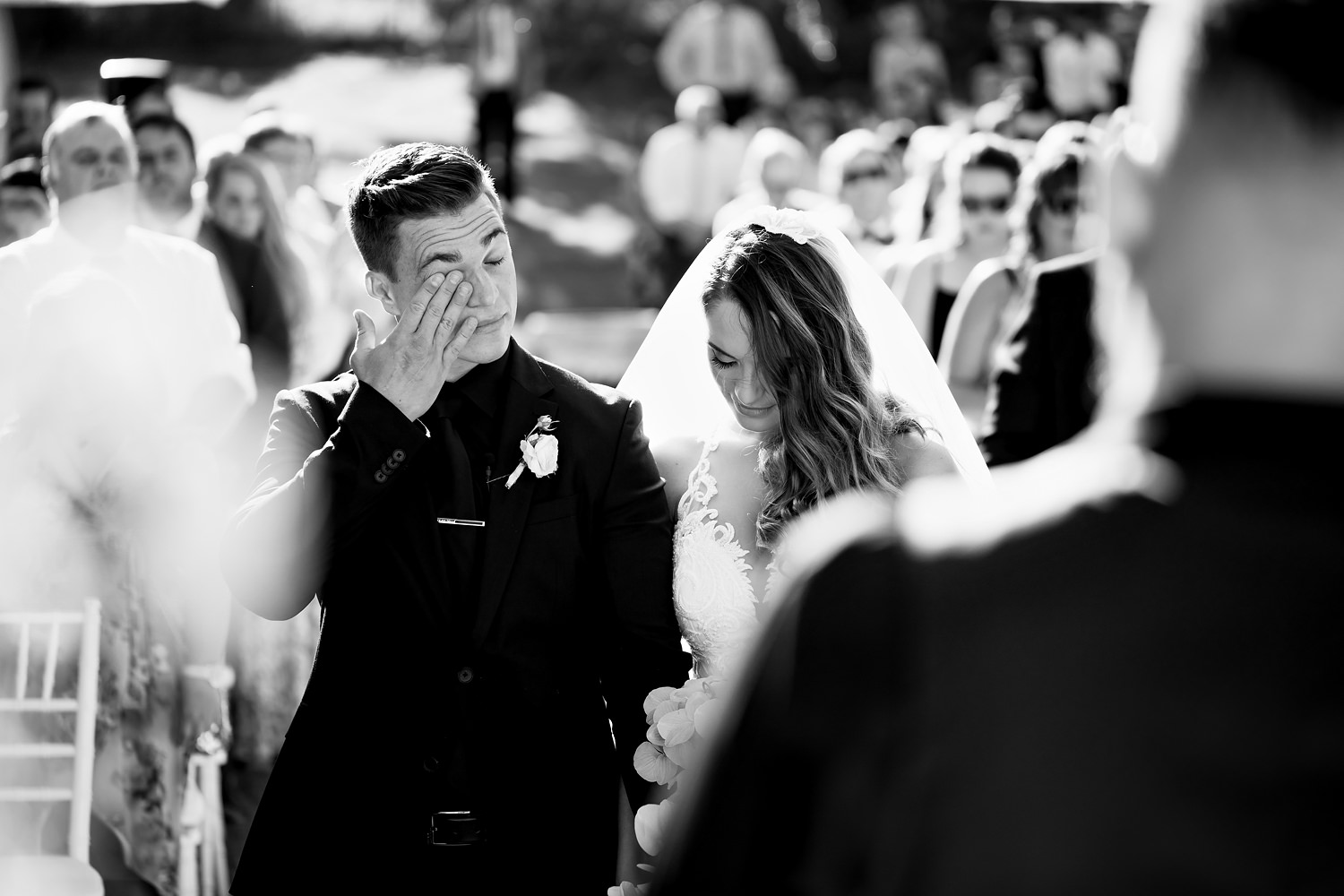 The groom, dressed in all black, wipes a tear away during a ceremony prayer. Captured by wedding photographer in South Africa, Niki M Photography
