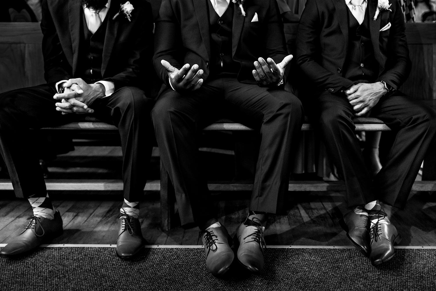 Three groomsmen sit in symmetry during the ceremony prayer, the middle one with palms up in praise.