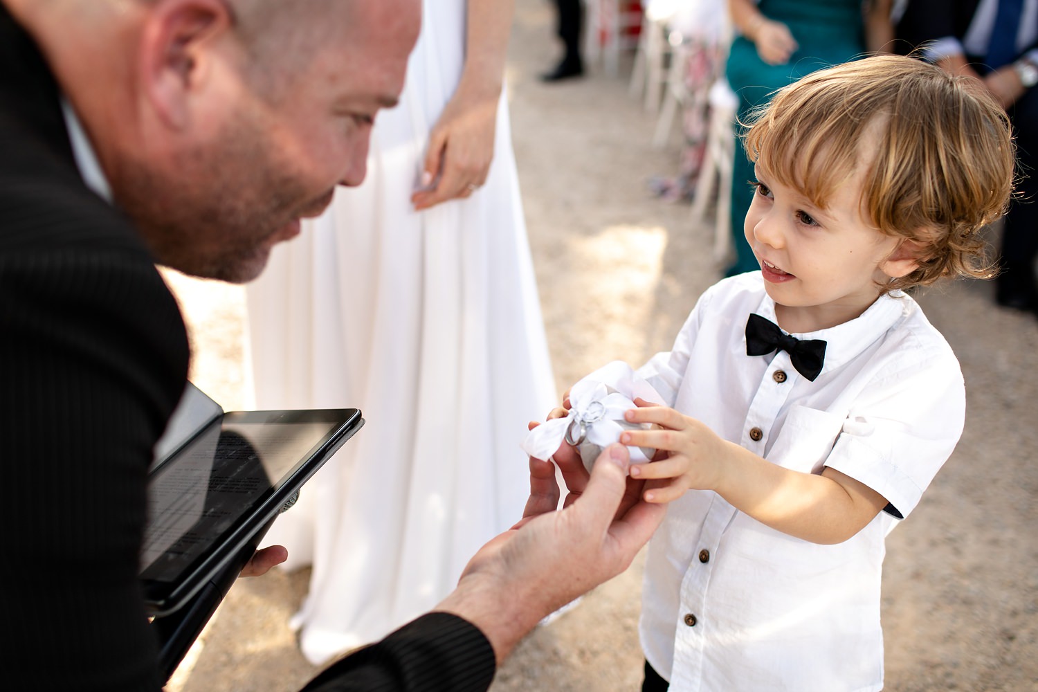 A cute little ringbearer with bowtie delicately hands the ring box to the wedding officiant by wedding photographer in South Africa, Niki M Photography