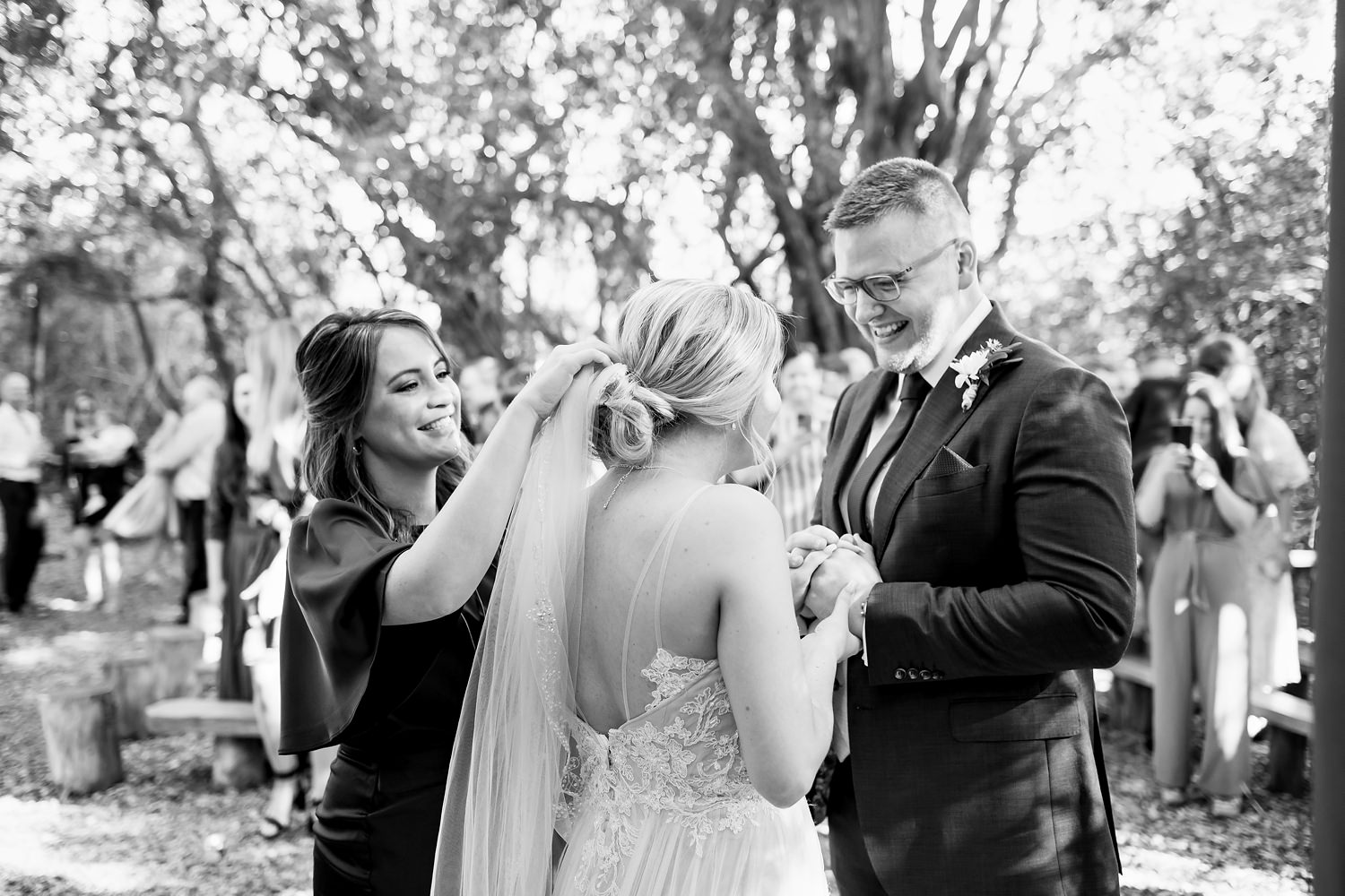 An elated bride and groom share a moment together after the ceremony whilst a bridesmaid fixes the veil. Image by wedding photographer in South Africa, Niki M Photography