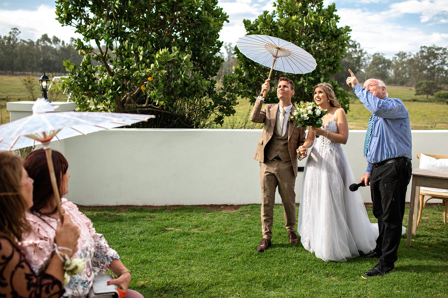 A groom holds a paper parasol over the bride's head as the minister points up at inclement weather at their wedding in the Eastern Cape, South Africa