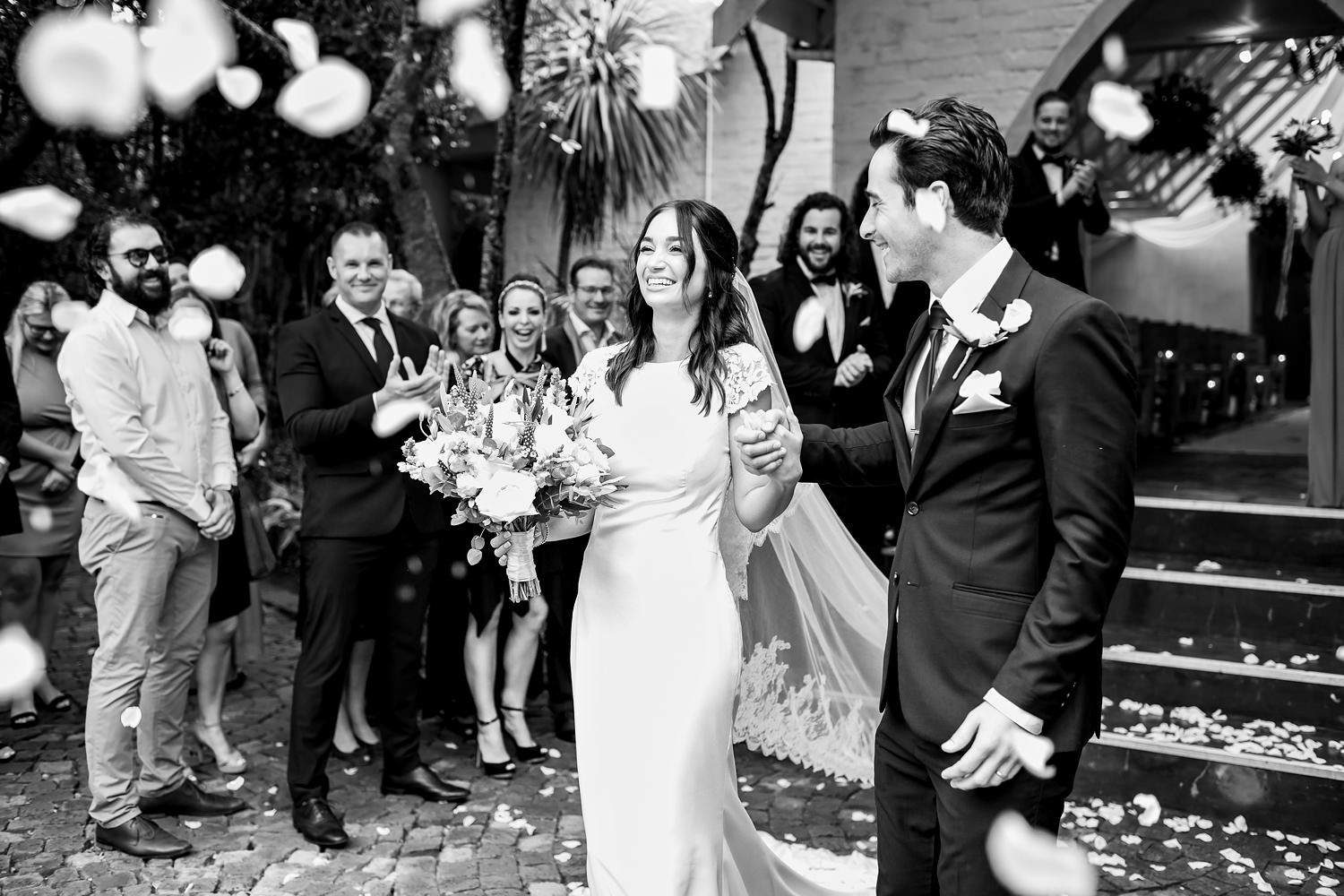 The bride and groom are showered with white rose petals after their wedding ceremony at The Plantation, captured by wedding photographer in South Africa, Niki M Photography