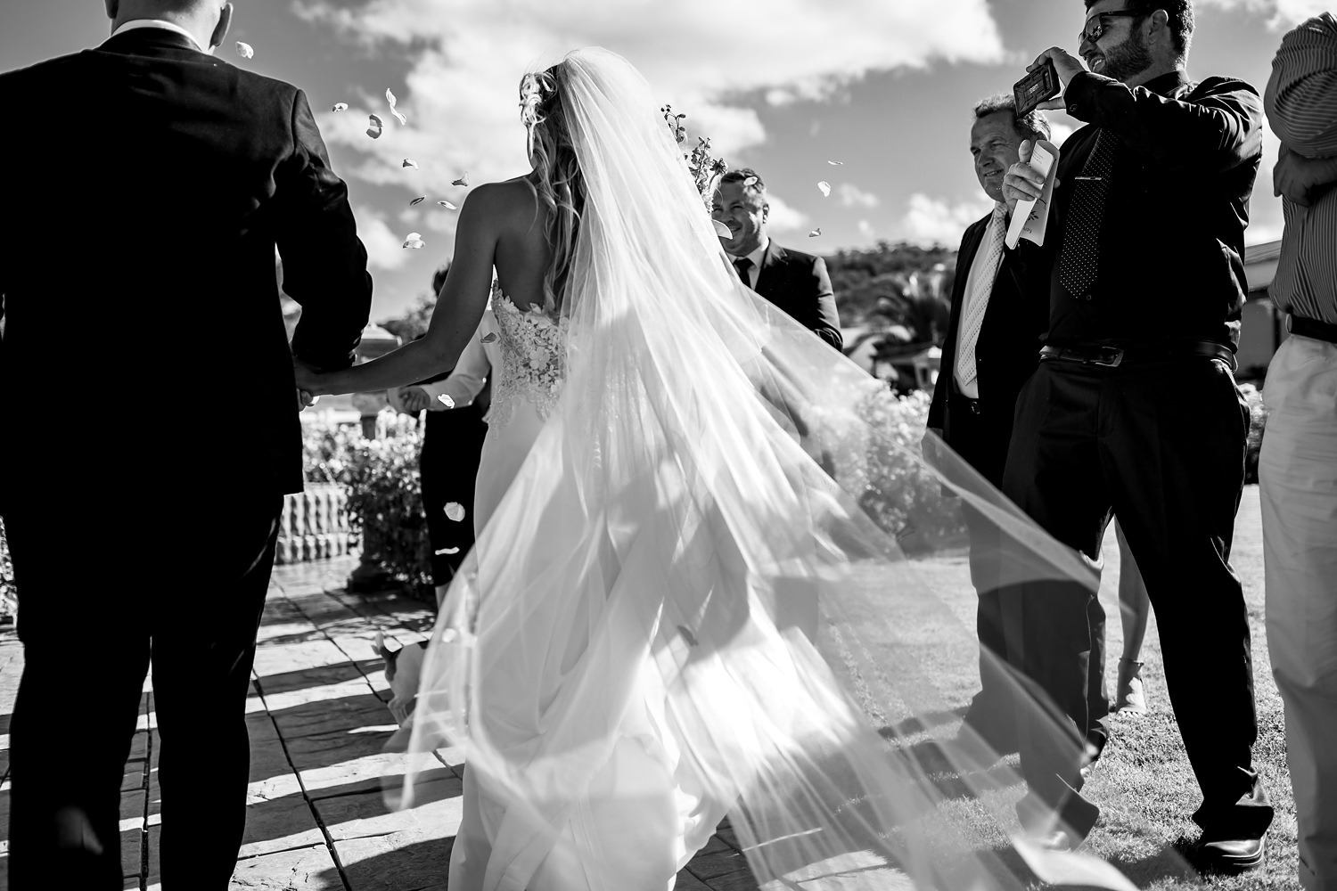 The bride's veil trails out after her as she makes her way down the line of guests throwing confetti