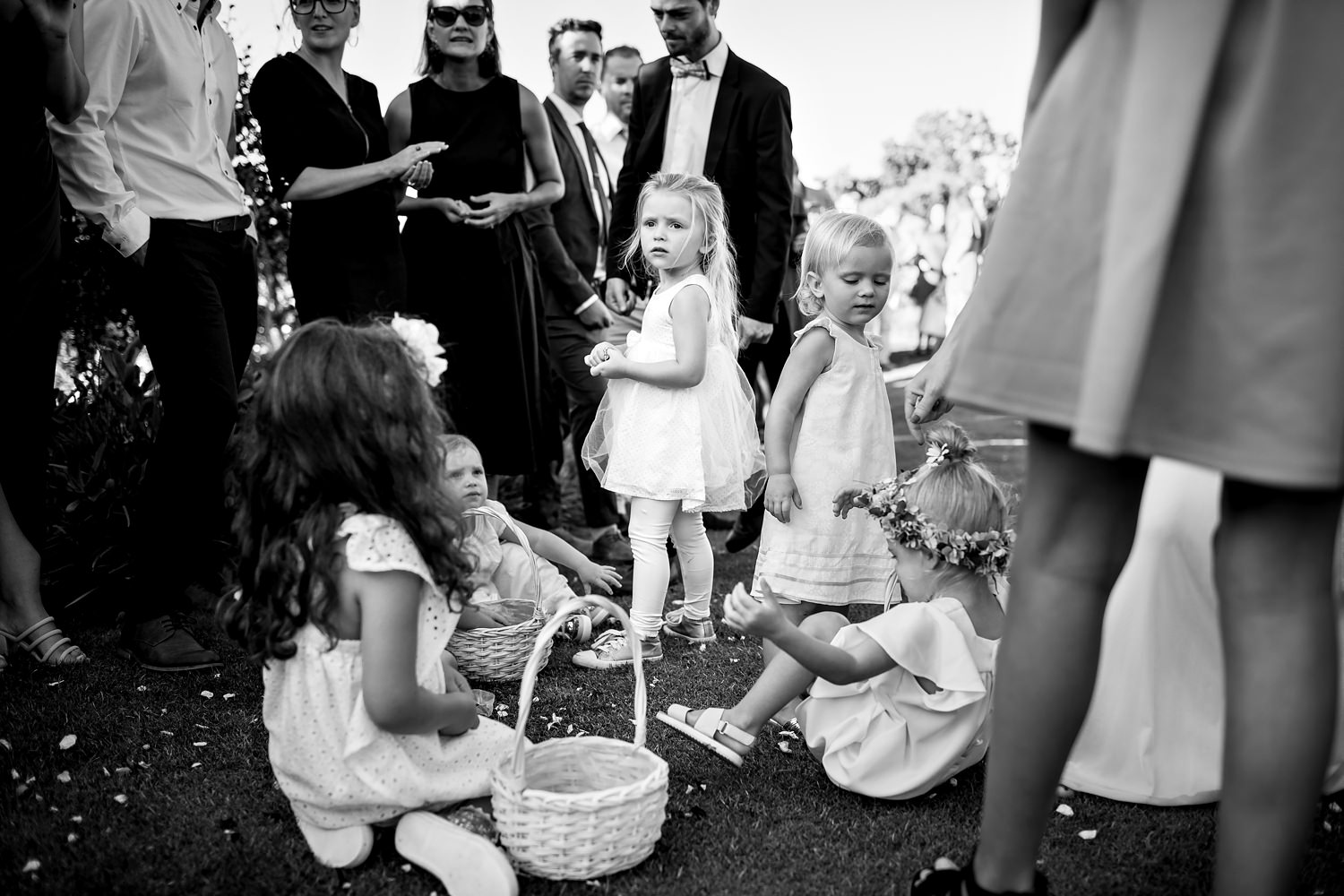 A group of flowergirls with baskets gather together amongst the guests and pick up petals to play with by wedding photographer in South Africa, Niki M Photography