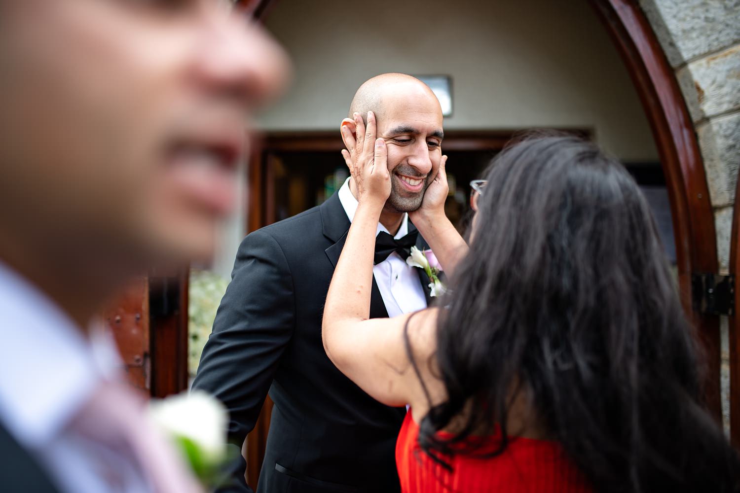 The groom's sister affectionately squeezes his face in her hands whilst congratulating him by wedding photographer in South Africa, Niki M Photography