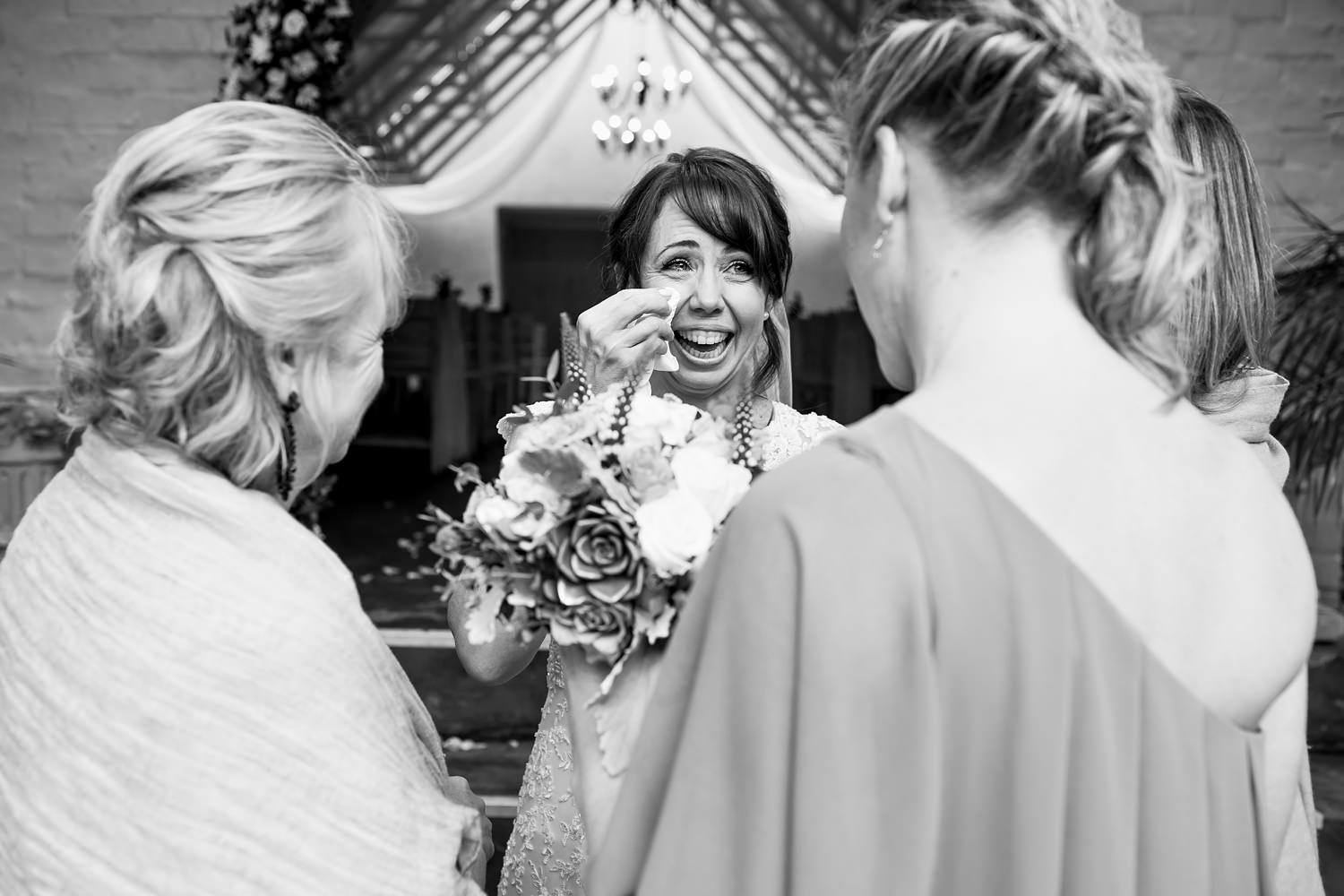A smiling and overhwelmed bride dries her tears whilst her bridesmaids and friends encircle her post wedding ceremony by wedding photographer in South Africa, Niki M Photography