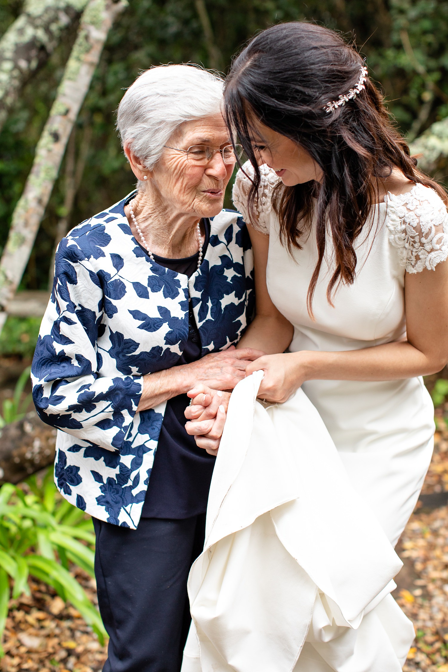 A bride and her grandmother share a joke and embrace during family photos
