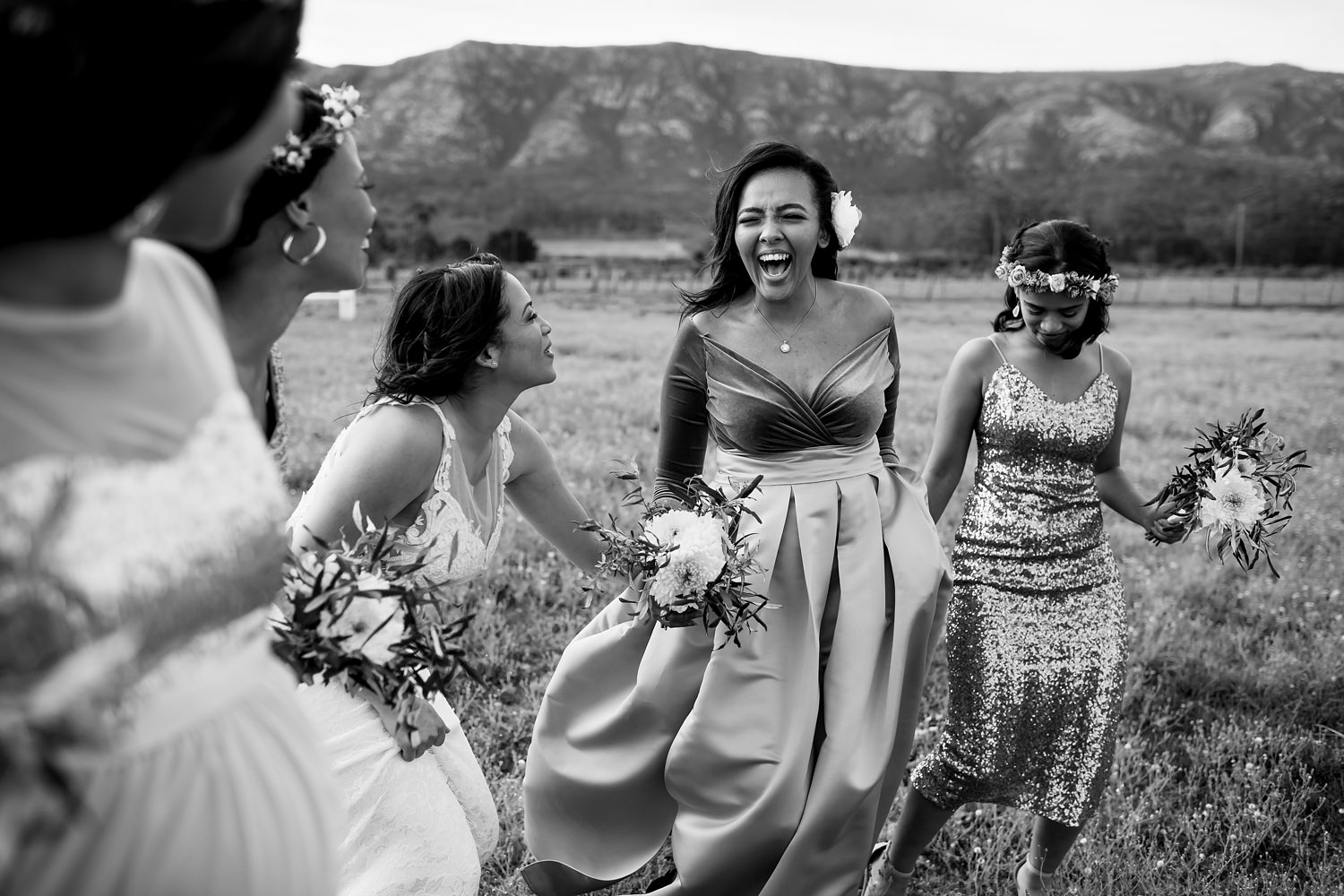 Playful bride and her bridesmaids during their entourage photo shoot in a field by wedding photographer in South Africa, Niki M Photography.