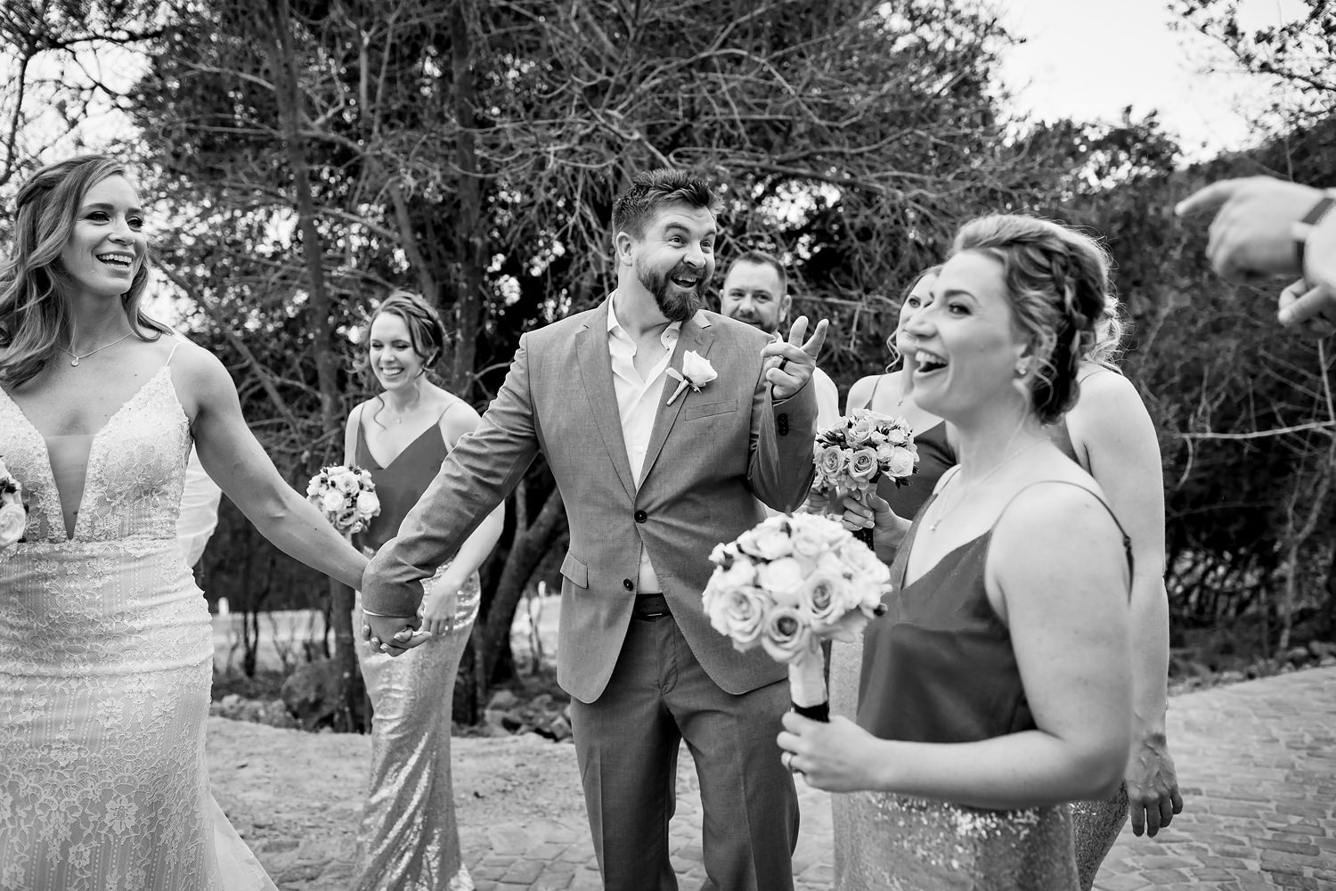 The groom walks and laughs with members of the bridal party in this natural black and white photograph by wedding photographer in South Africa, Niki M Photography