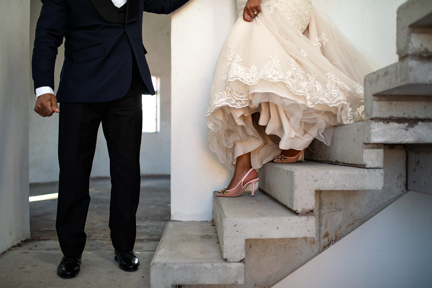 The groom helps the bride down concrete stairs during their wedding photography session by wedding photographer in South Africa, Niki M Photography