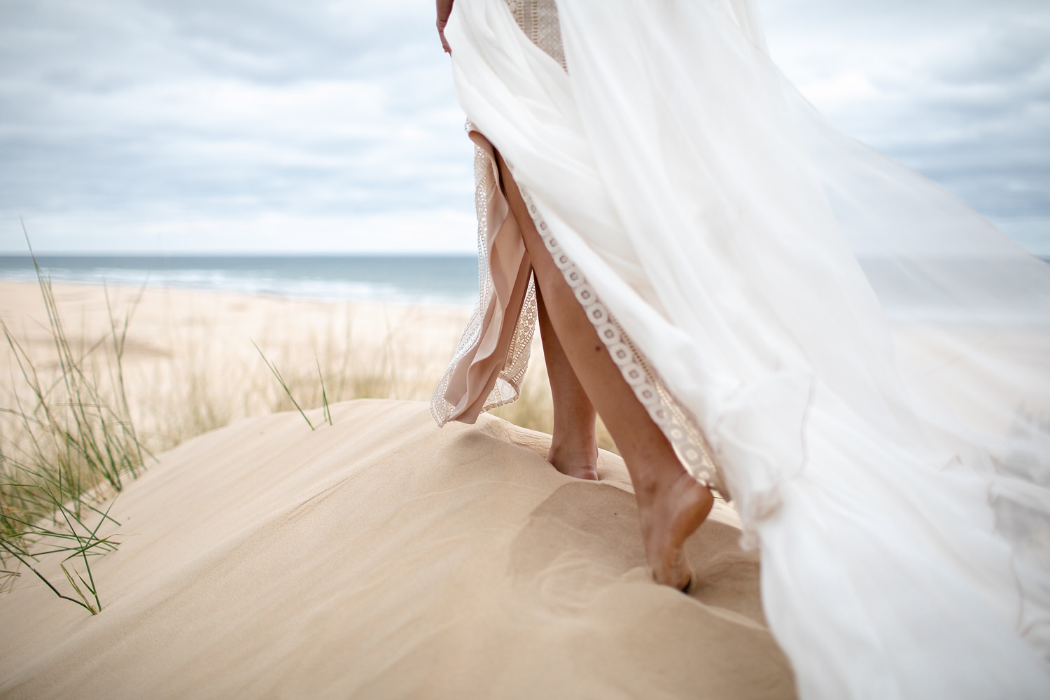 Photograph of a bride walking in the sand on top of a dune on her wedding day at Oceana, with her wedding dress trailing in the breeze. Photo by wedding photographer in South Africa, Niki M Photography