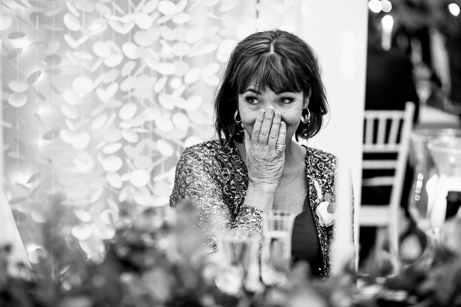 Mother of the bride wears a sequin top and laughs during the wedding speeches
