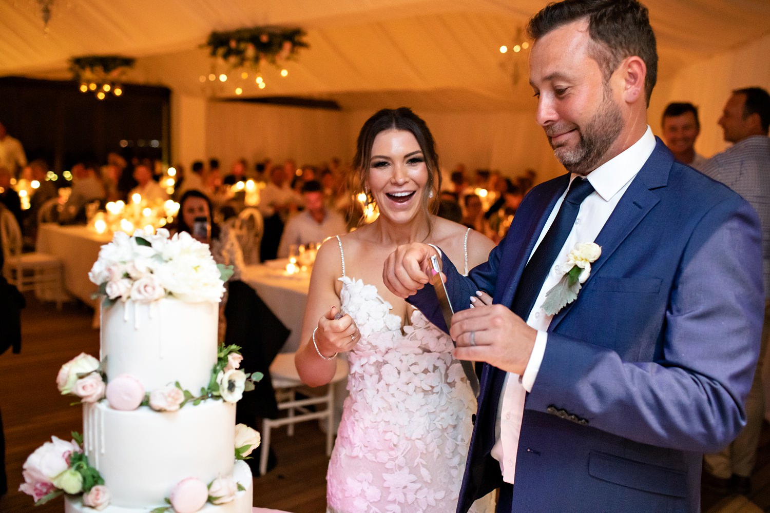 Bride laughs at groom who broke the knife whilst cutting the classic wedding cake with macarons at their wedding reception at St Francis Links