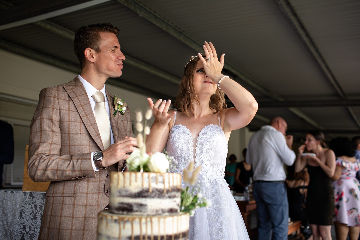 Bride wipes her nose in an upward motion after groom smears cake on her face during canapes after the wedding ceremony at Andante wedding venue