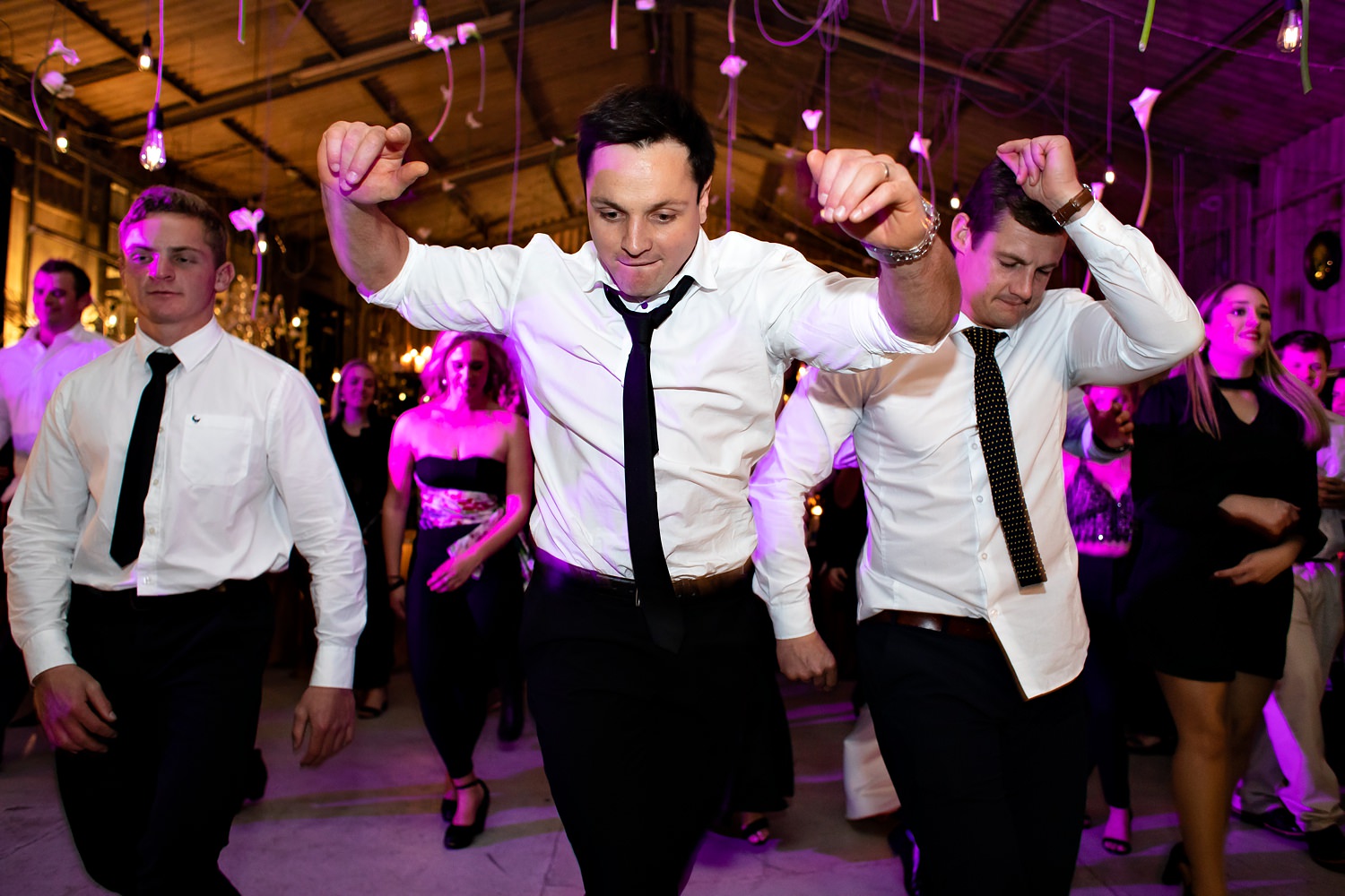 South African wedding guests dance to cha cha slide as pink parquet lights illuminate the background in this image by wedding photographer Niki M
