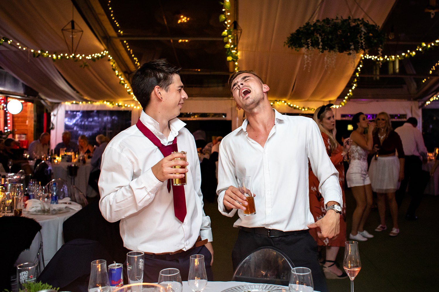 A wedding guest sings loudly whilst another guest looks at him quizzically whilst holding a drink