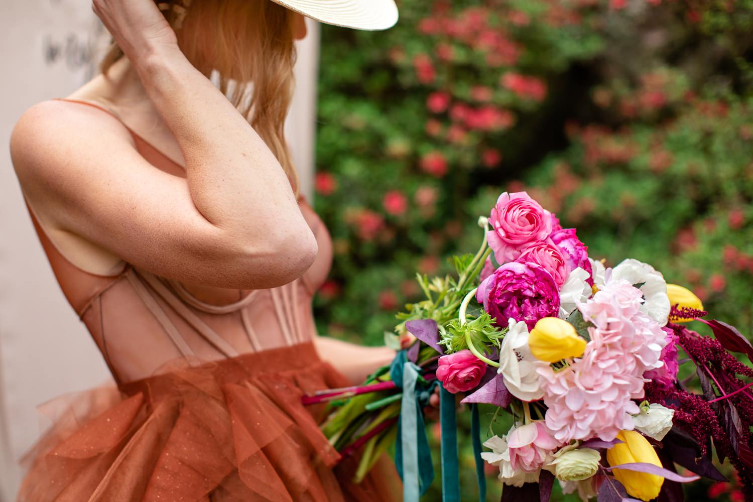 The blonde bride with loose fishtail braid models a colourful bouquet with anemones, country roses and tulips, and an alternative burnt orange wedding dress with straw hat.