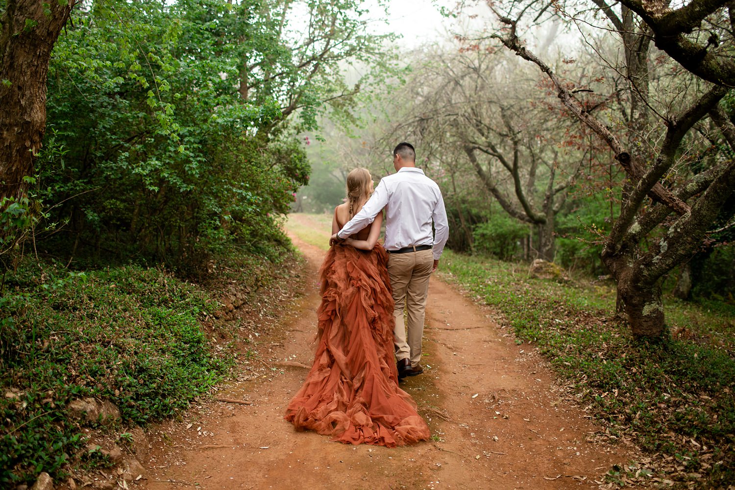 The bride and groom walk down a tree-lined dirt road at their elopement at Cheerio Gardens in Magoebaskloof