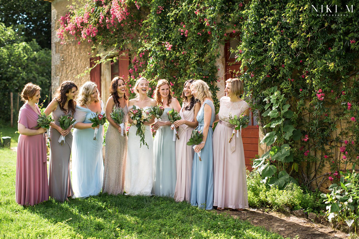 Bridesmaids in front of old stone building with rambling roses at Chateau de la Bourlie Dordogne wedding venue