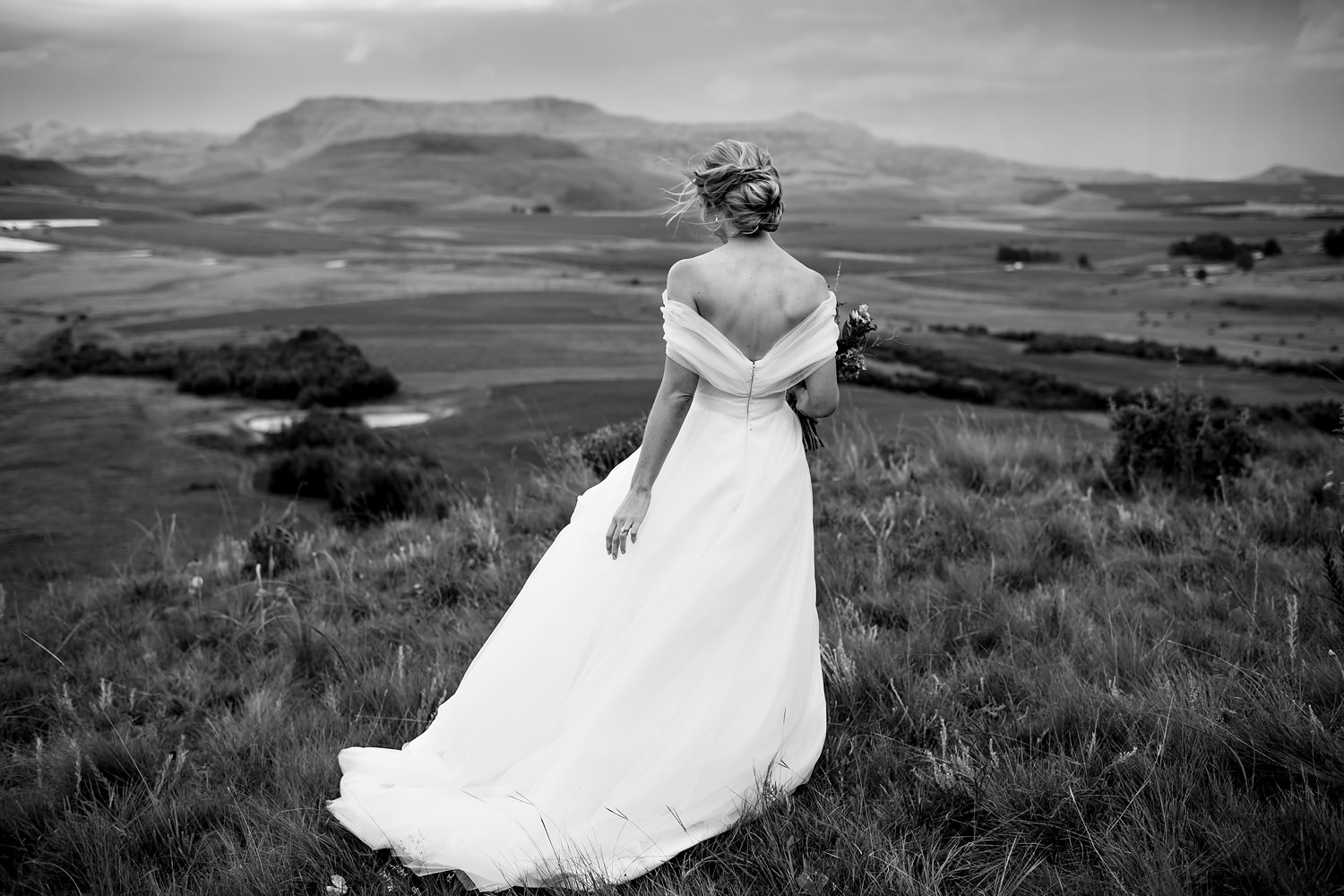 A bride walks away from the camera after her Drakensberg wedding ceremony in this black and white image by Niki M Photography.