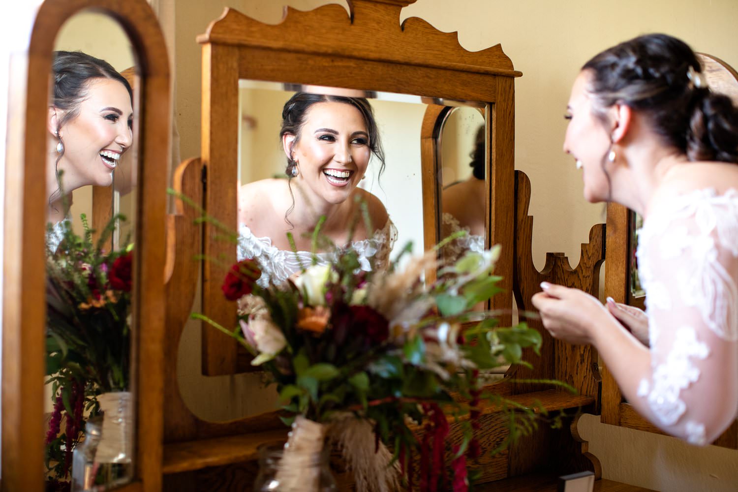The bride laughs into a mirror as she puts on her earrings whilst preparing for her wedding in Elgin