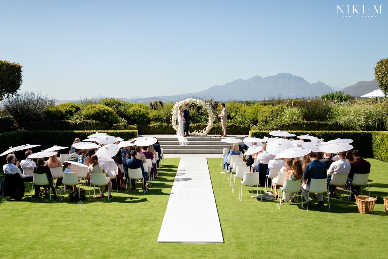 Cavalli Estate wedding in the sunken garden with white rose floral arch, and cape town's helderberg mountains in the background