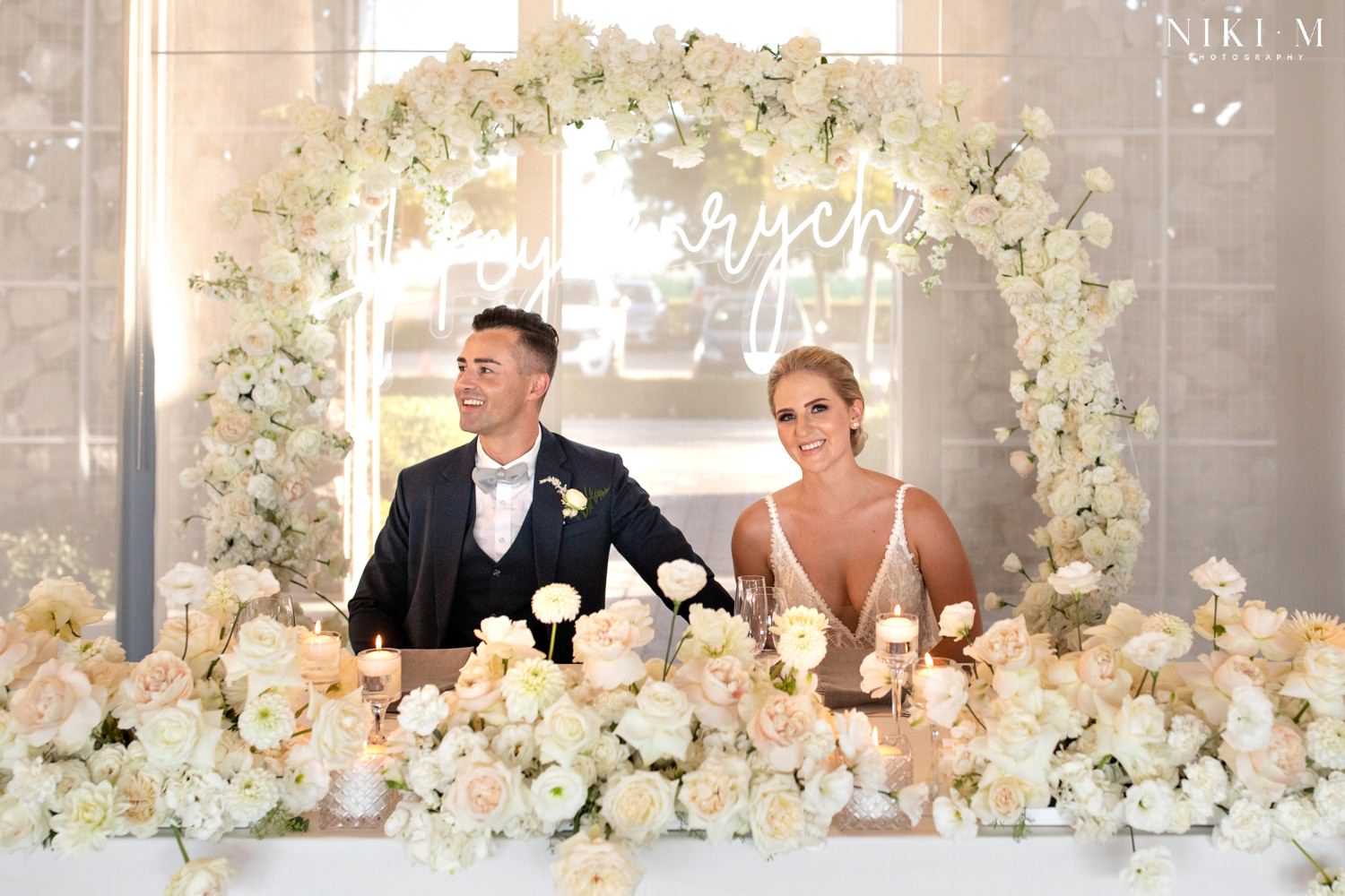 White bridal table floral arrangements with roses and a neon surname sign