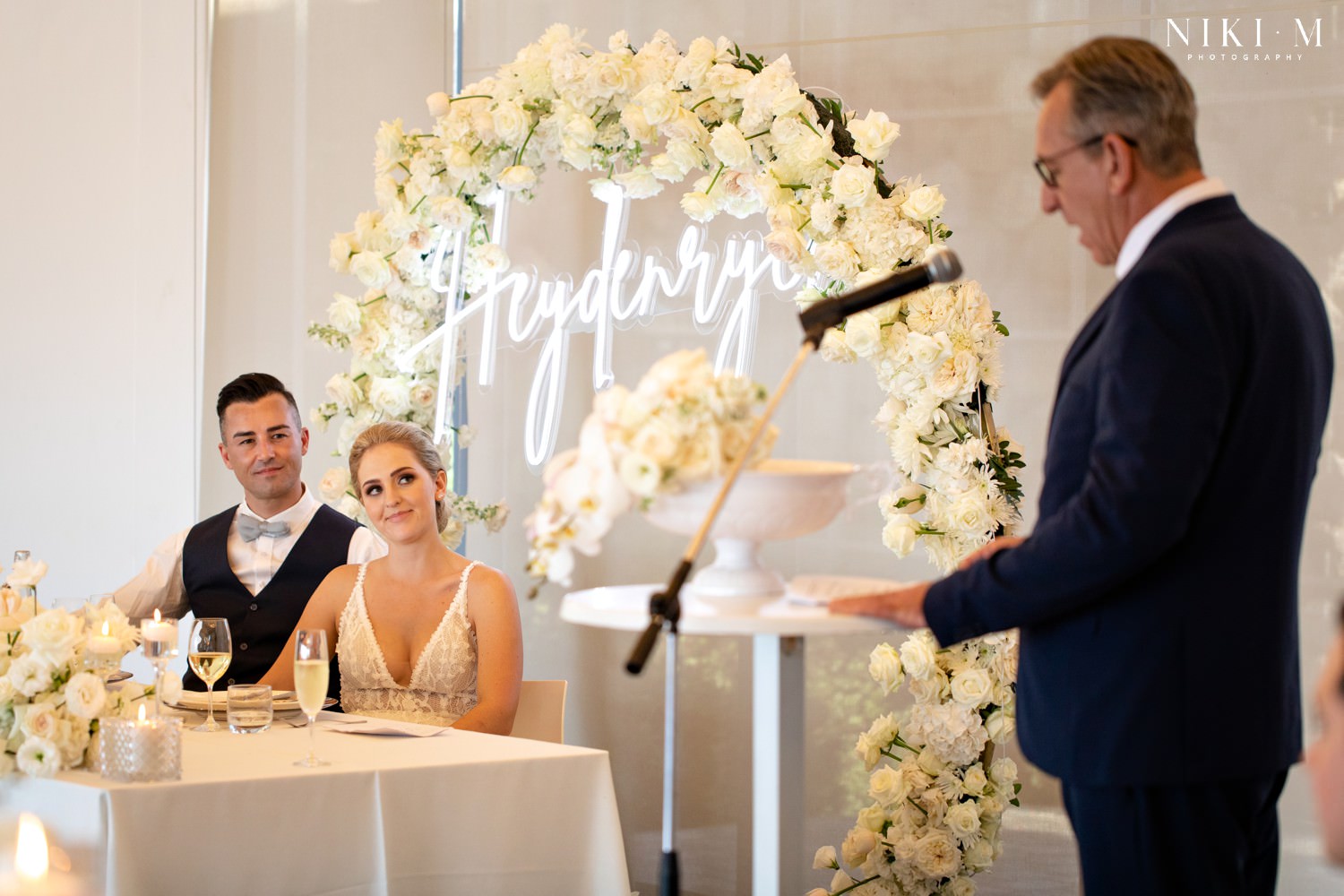 White wedding floral arrangements with roses and a neon surname sign