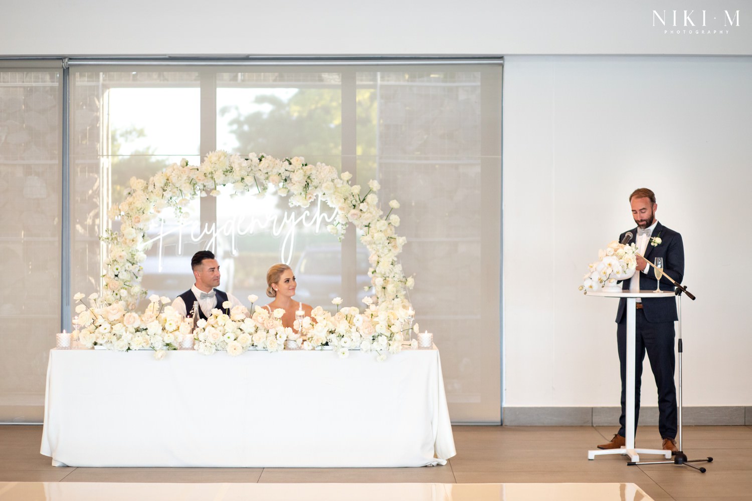 White bridal table floral arrangements with roses and a neon surname sign