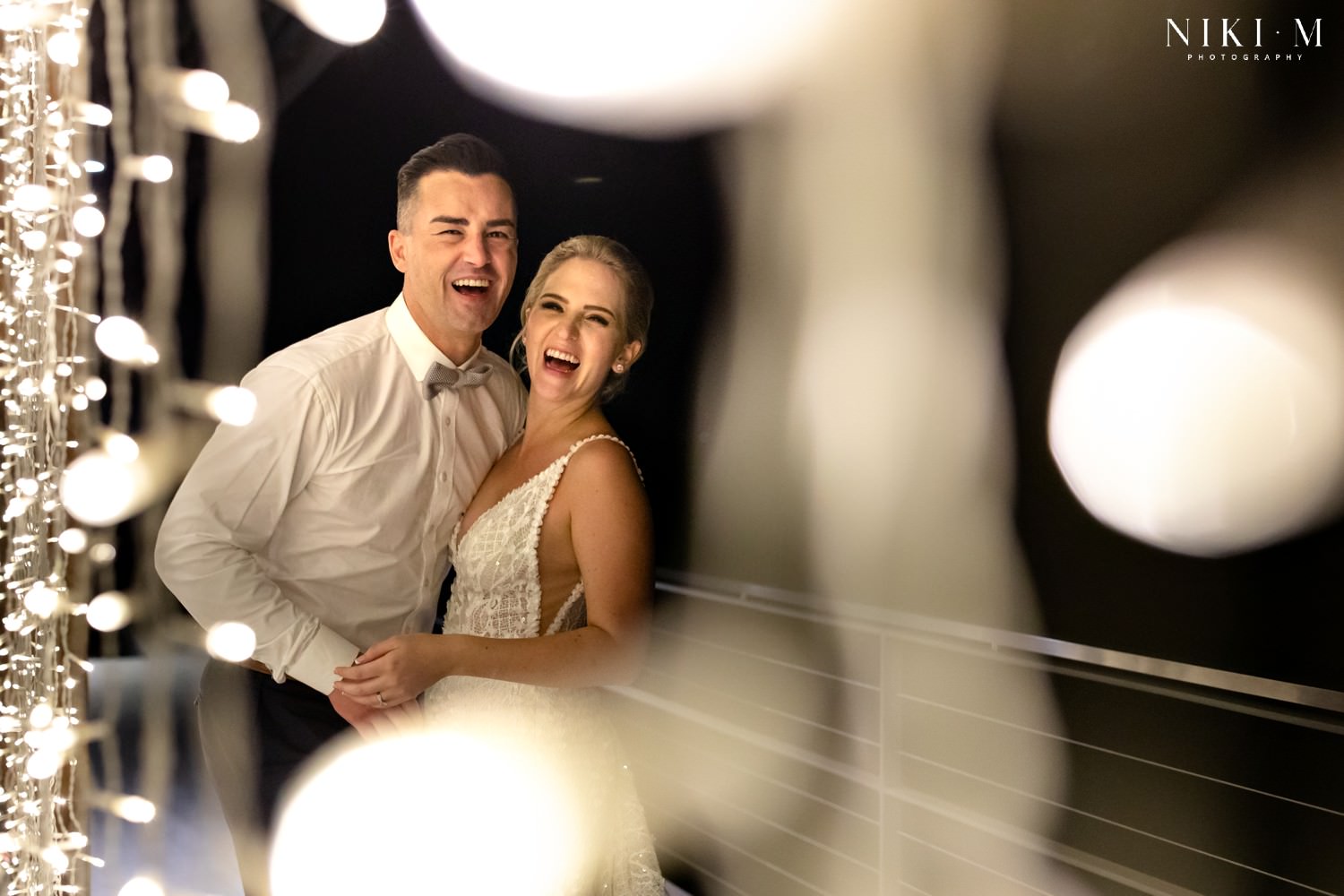 The bride and groom are photographed through the fairy lights at the end of the evening after their Cavalli estate wedding in the cape town winelands
