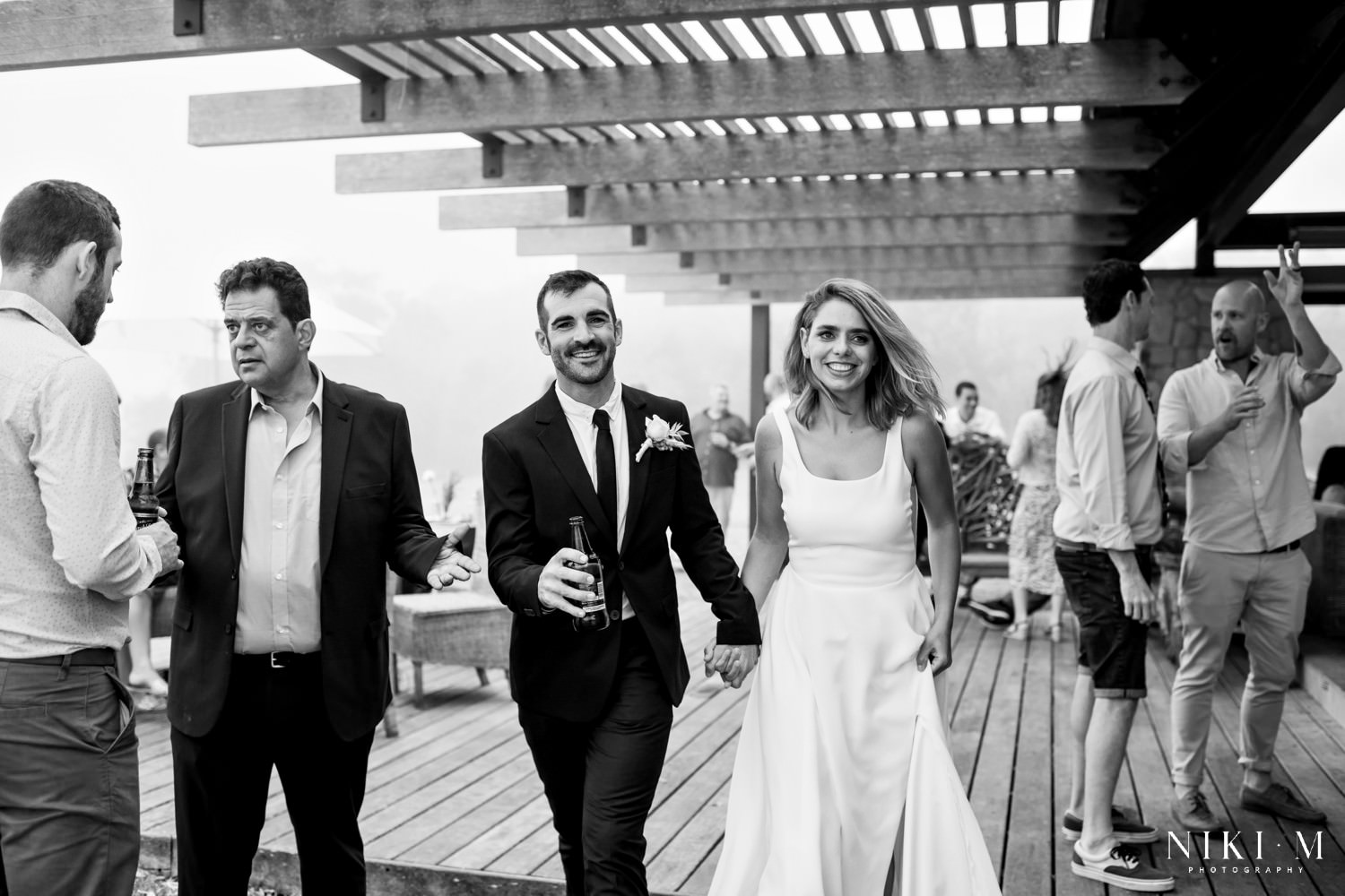 Lexi and Luke, the bride and groom, hold hands and walk between their guests during canapés.