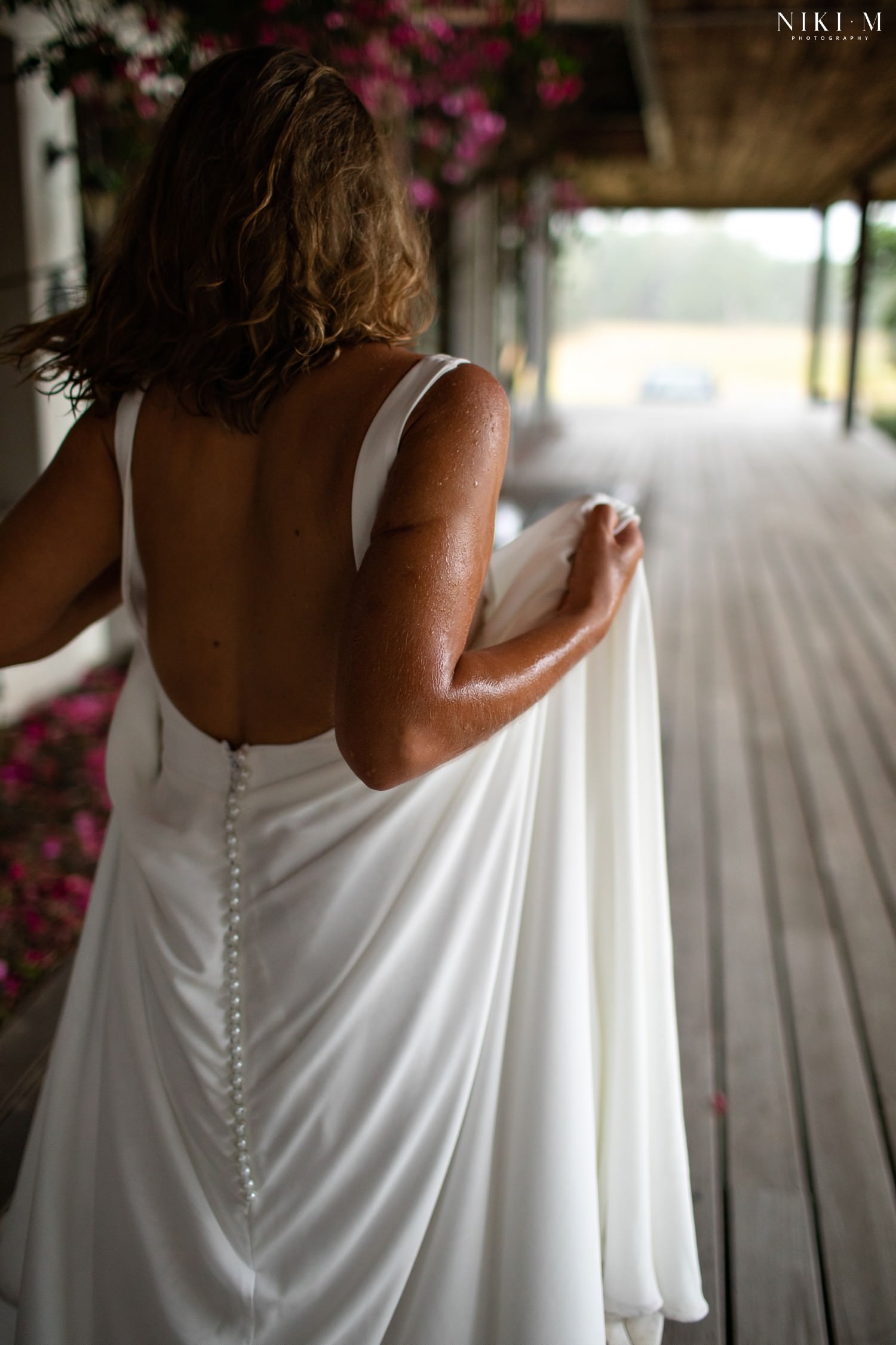 The bride takes shelter as the heavens open and rain pours down on her wedding day. He arms are wet as she walks away from the camera.