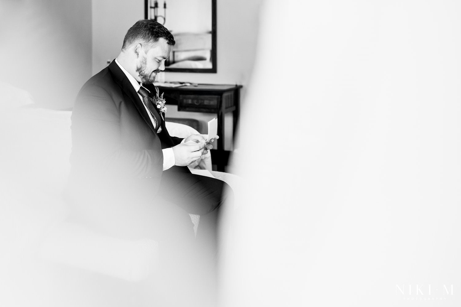 The groom sitting quietly on the edge of the bed reading a heartfelt letter from his bride, captured in soft light before their intimate Drakensberg micro-wedding ceremony.