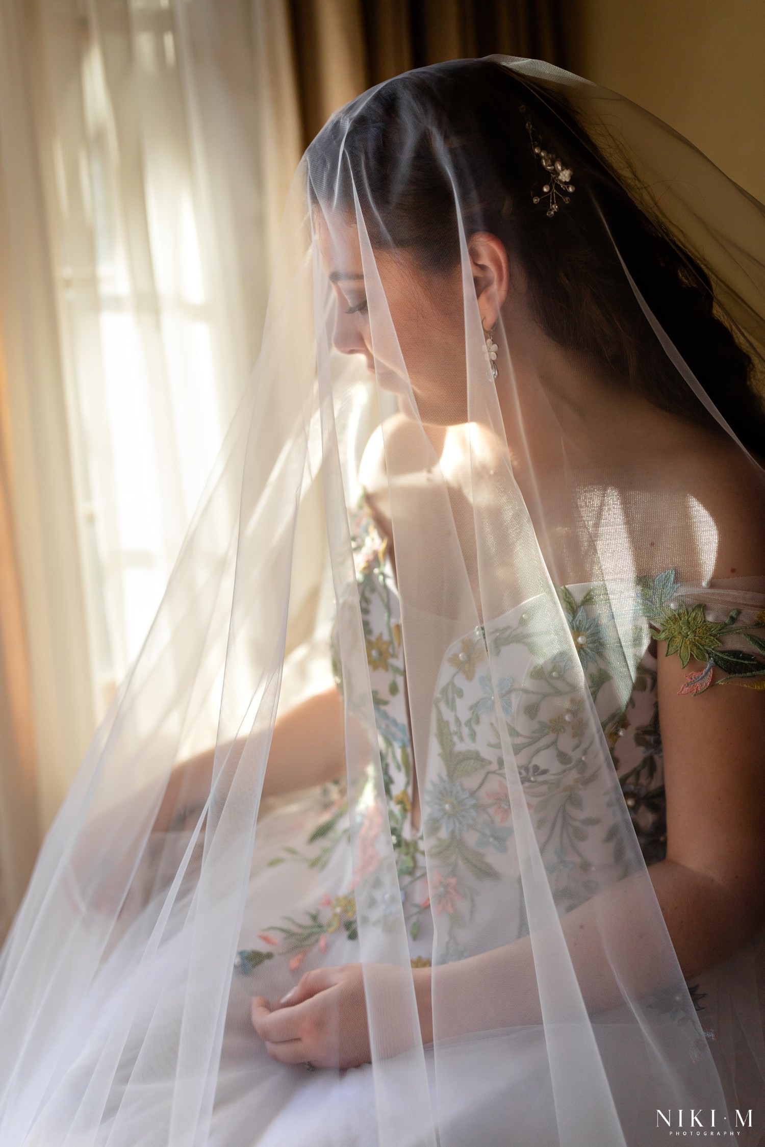 A soft, dreamy portrait of the bride under her veil with sunlight streaming through, highlighting the floral details of her gown — a serene moment from a romantic Drakensberg micro-wedding.