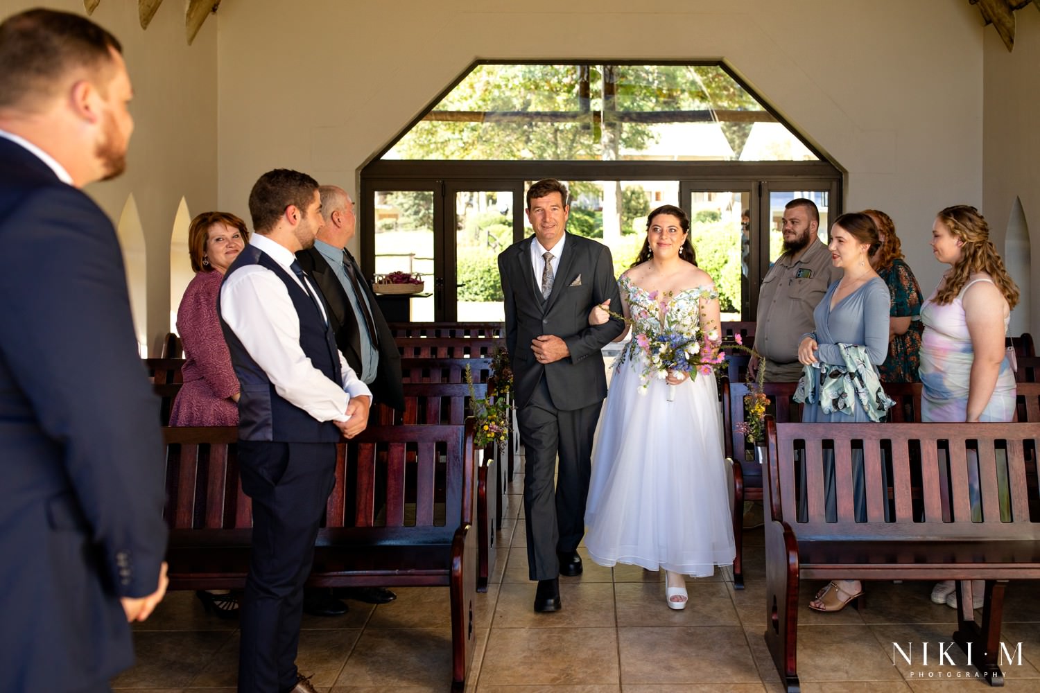 Bride walks down the aisle of the intimate Champagne Castle Hotel chapel, family and close friends watching during this heartfelt Drakensberg micro-wedding.