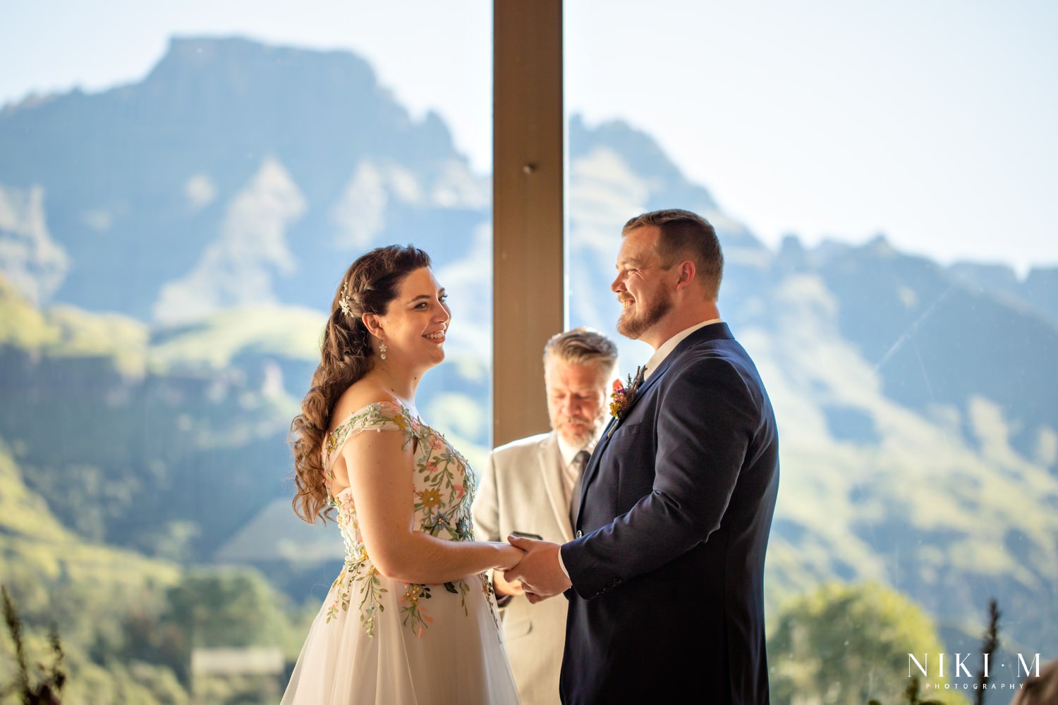 The couple exchange vows against a breathtaking view of the Drakensberg mountains framed by the chapel window at Champagne Castle Hotel.