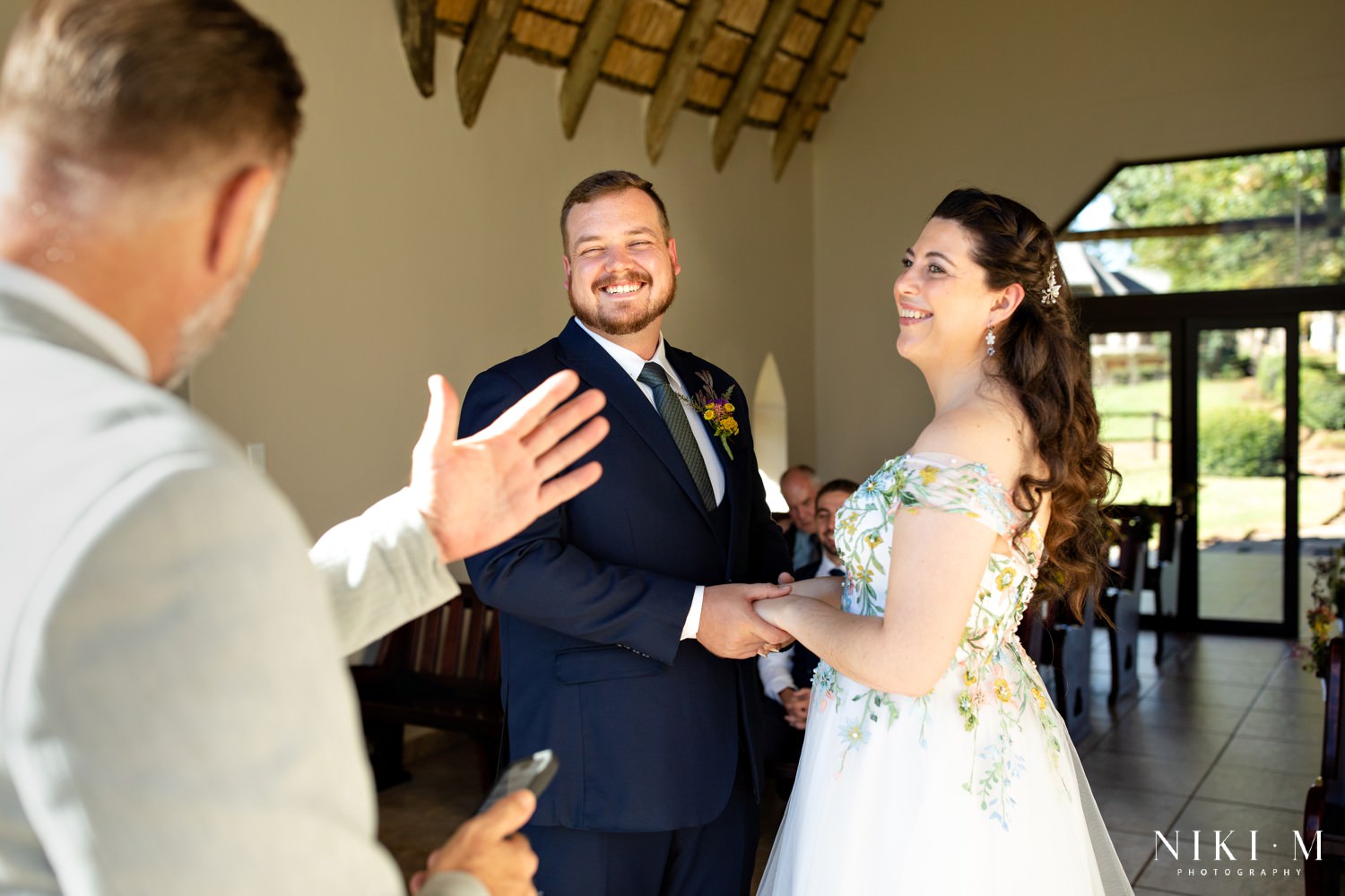 The officiant smiles as the bride and groom exchange vows, laughter filling the intimate chapel during their Central Drakensberg wedding ceremony.