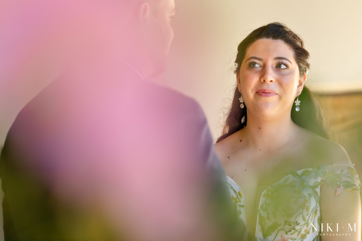 Bride’s emotional gaze as she looks at her groom during their vows in the Drakensberg, photographed through soft pink and green foregrounds for a dreamy feel.