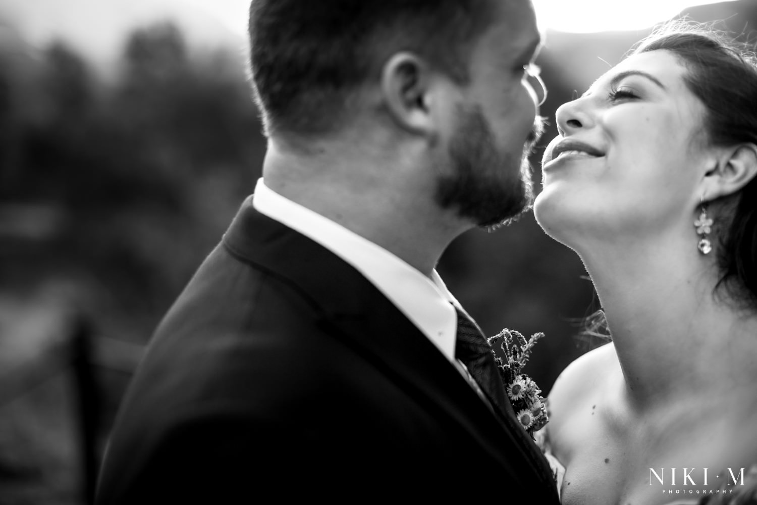 Joyful candid black and white image of the bride leaning toward her groom for a kiss, photographed in golden light with the Drakensberg mountains softly blurred in the background.