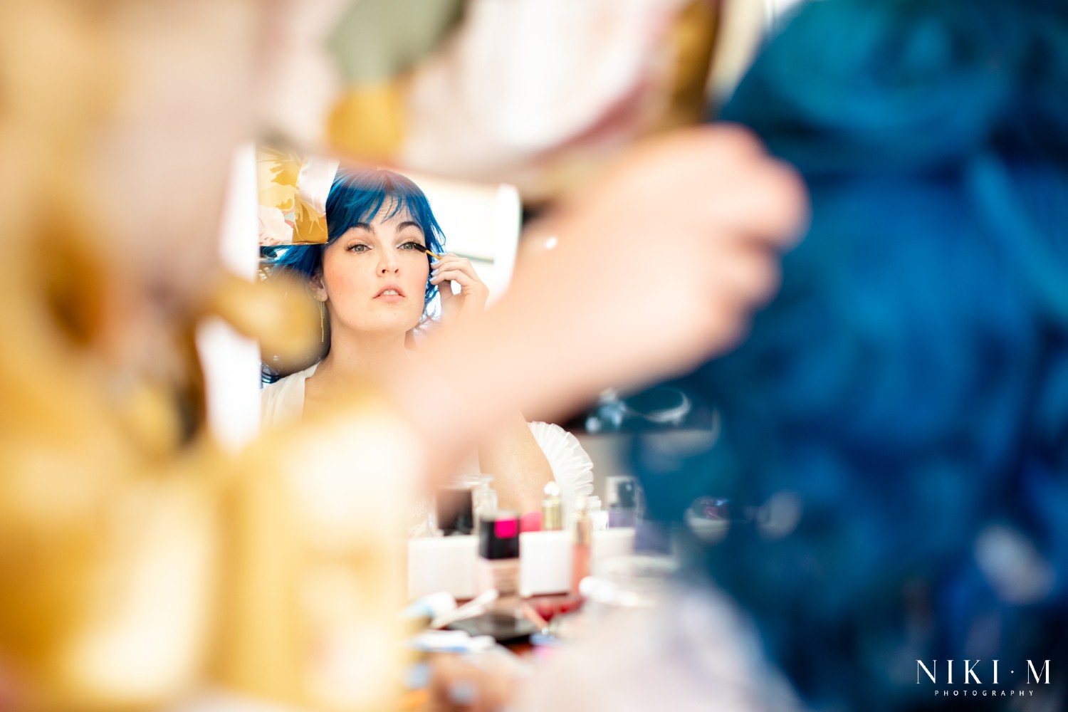 Bride applying her own makeup in the mirror, blue hair and flower crown, at a Drakensberg wedding