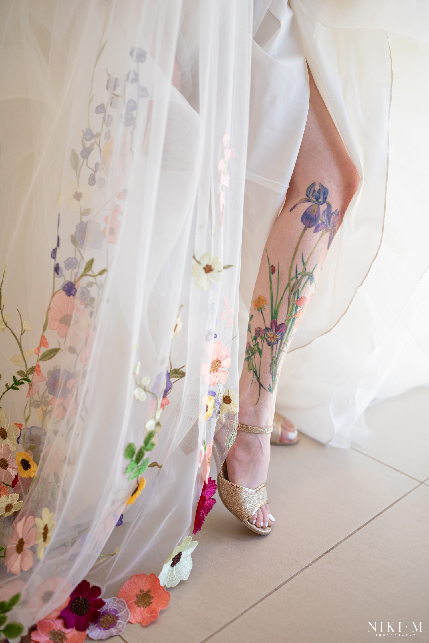 Hand-embroidered floral veil over the bride's wildflower leg tattoo and gold heels at a Drakensberg wedding